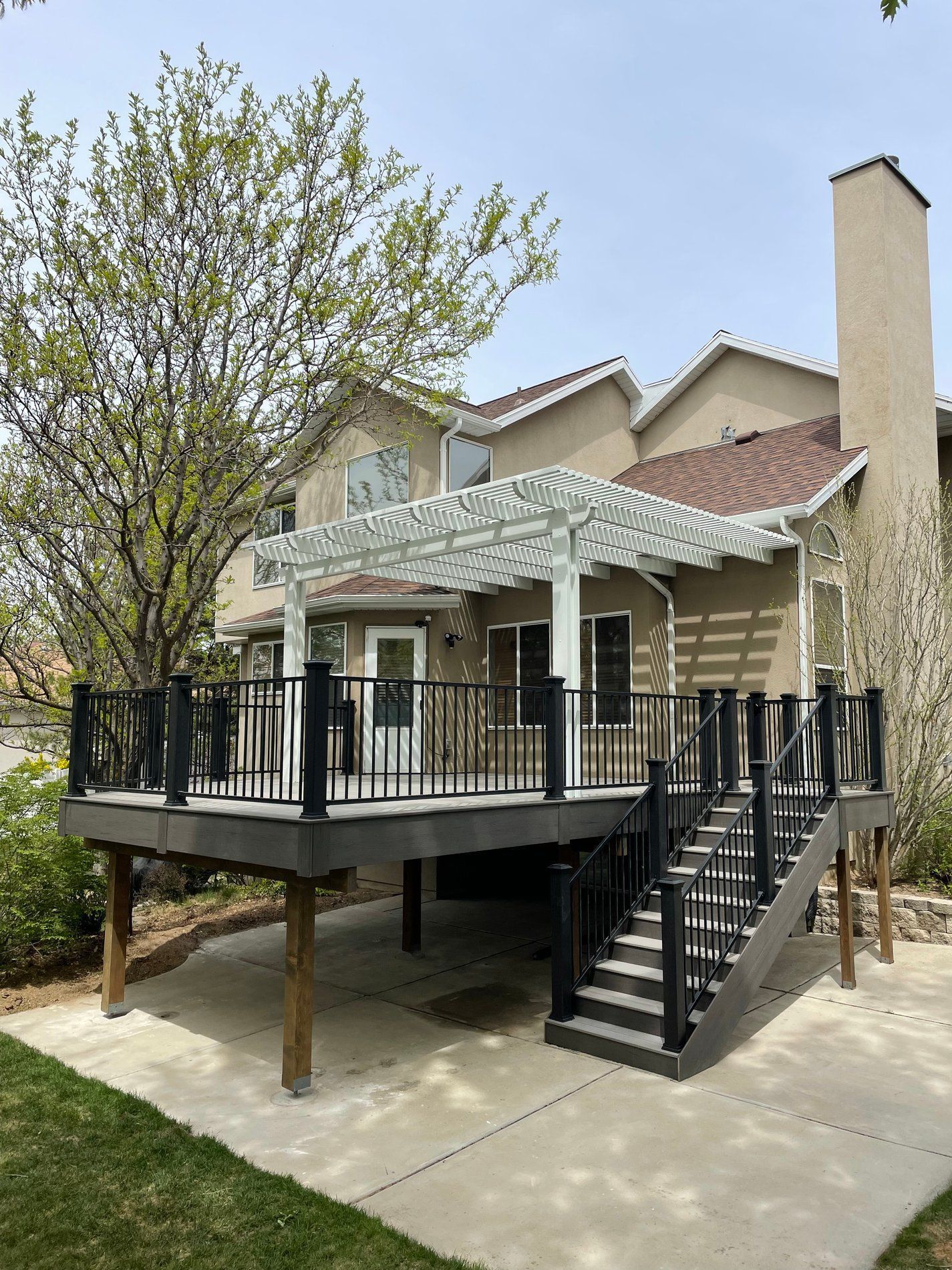 Backyard deck with black railing, stairs, and pergola beside a beige house under a tree