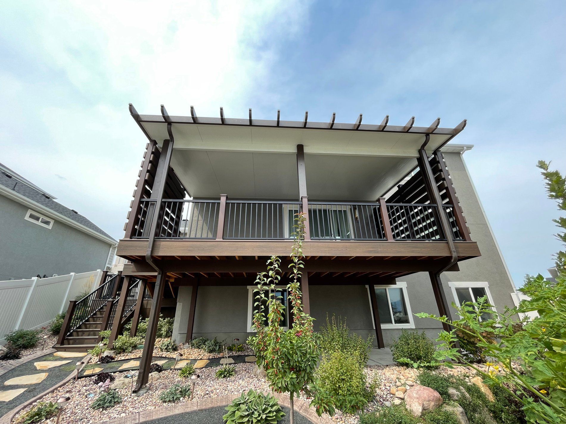 Modern two-story house with a covered balcony, wooden railings, and landscaped front yard