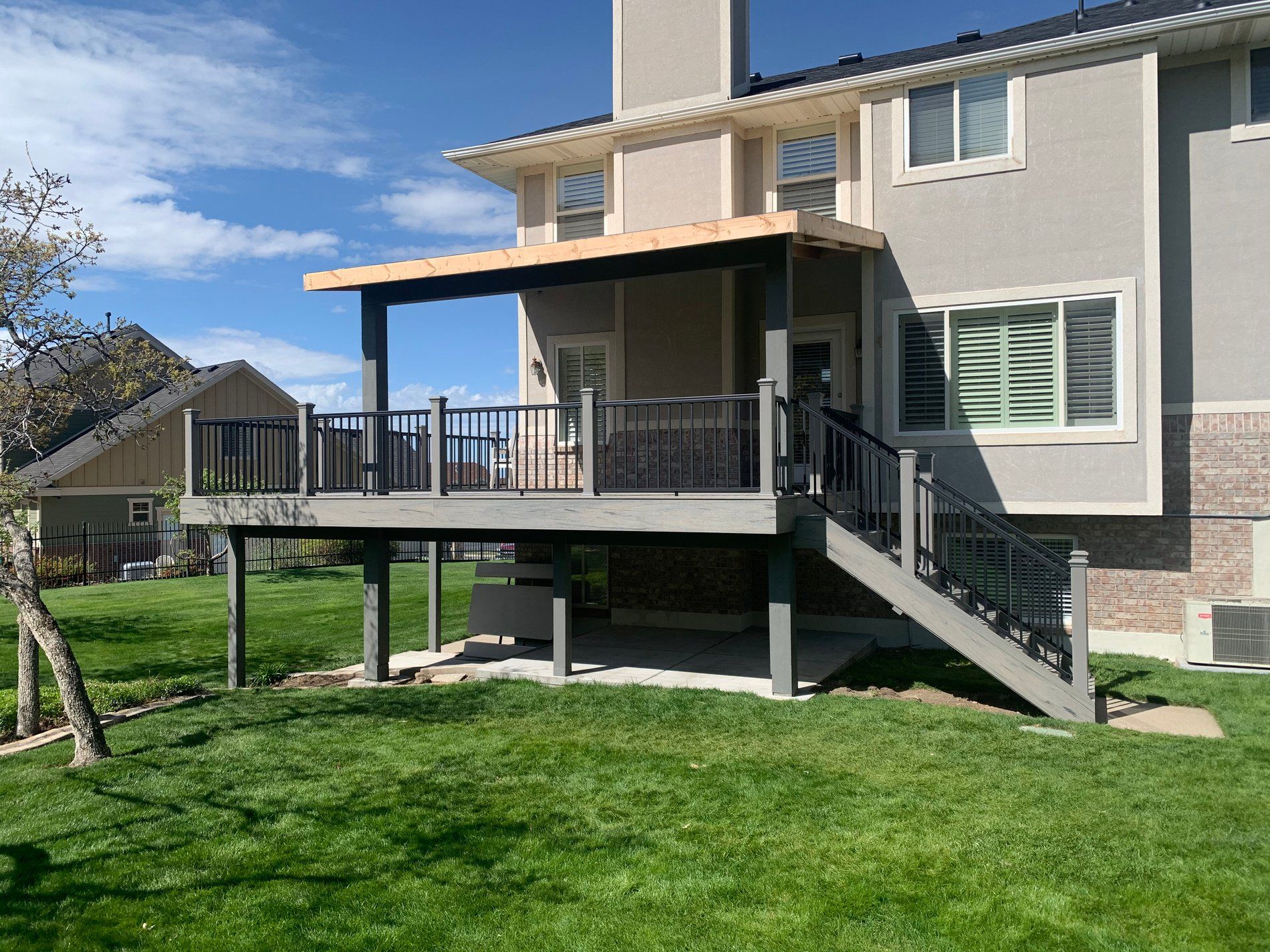 Back patio deck with stairs and railing on a two-story house over a green lawn