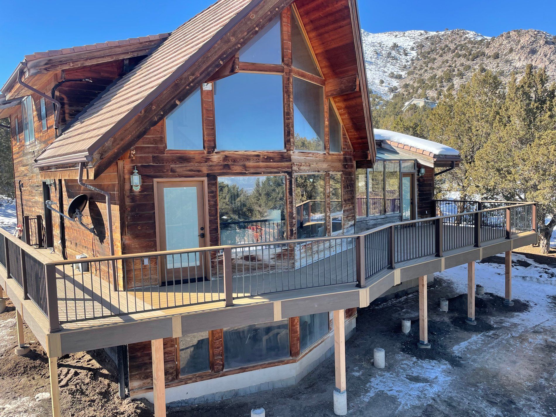 Modern wooden cabin with wraparound deck and large windows in a snowy mountain setting