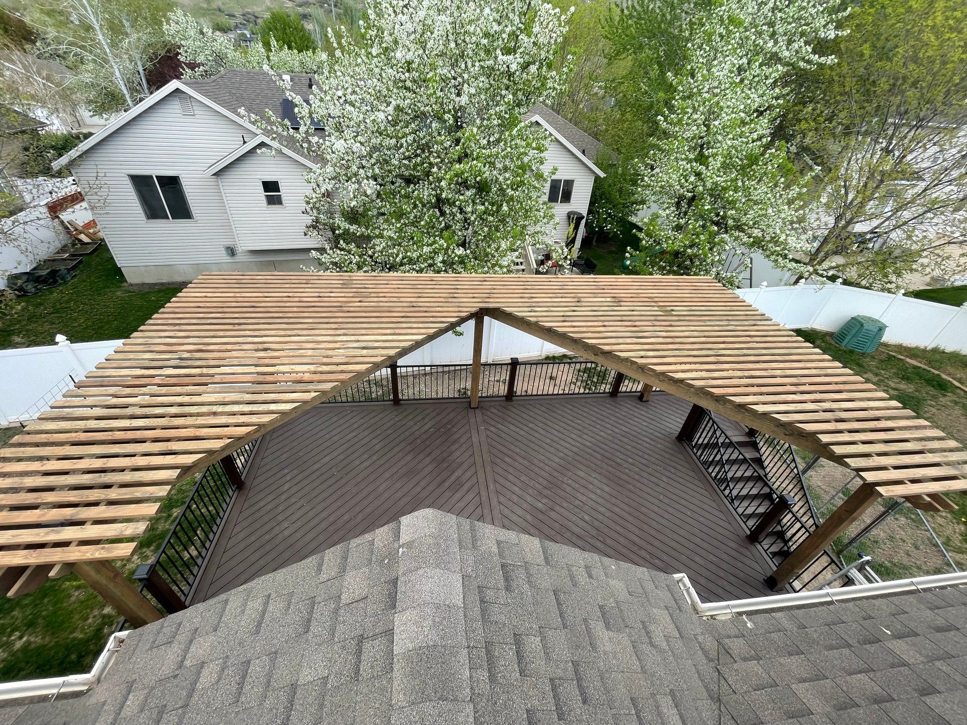 Backyard patio under construction with wooden roof framing and a shingled deck, surrounded by trees and neighboring houses