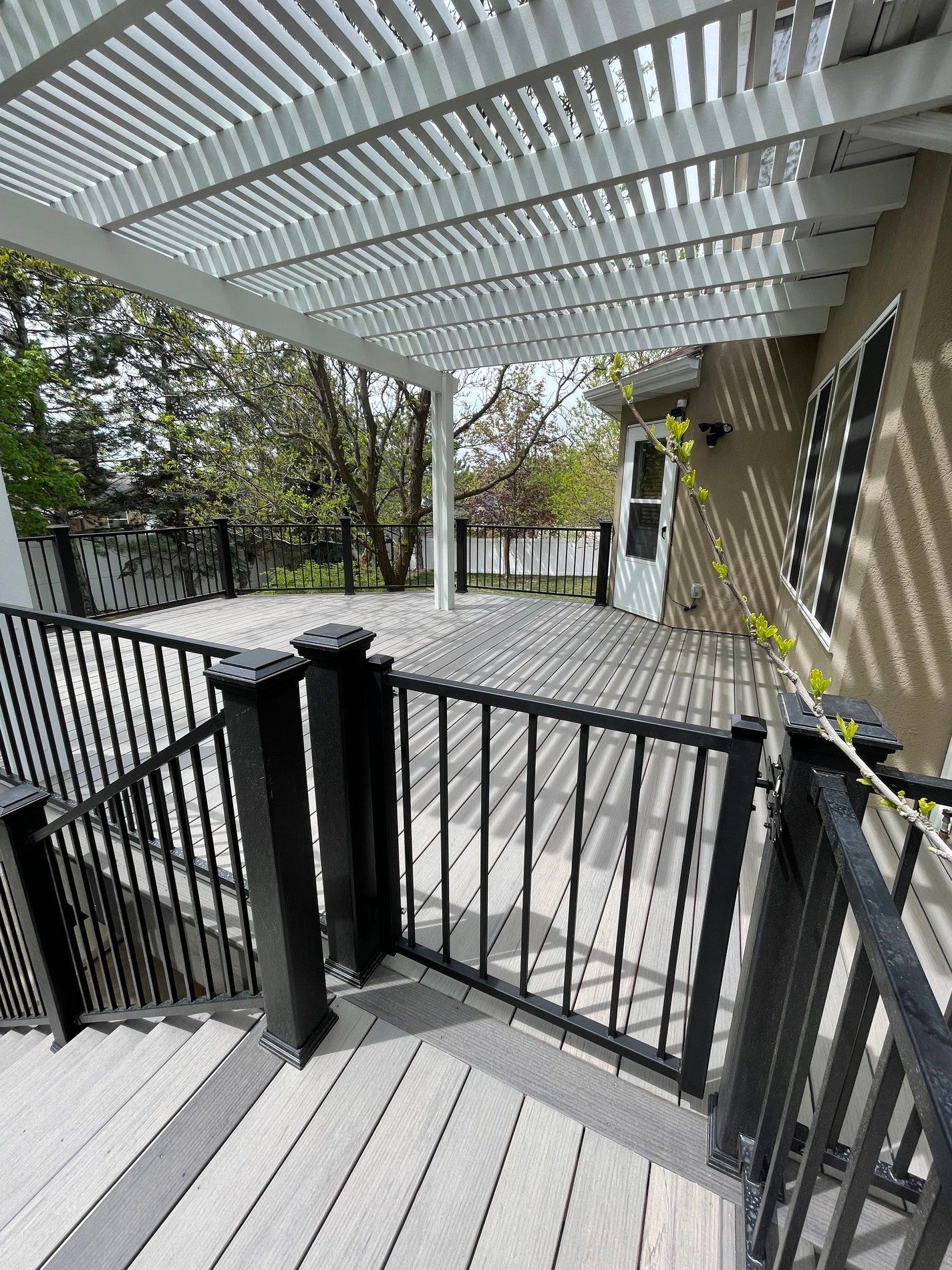 Covered patio with black railings, gray decking, and trees beyond the deck gate.