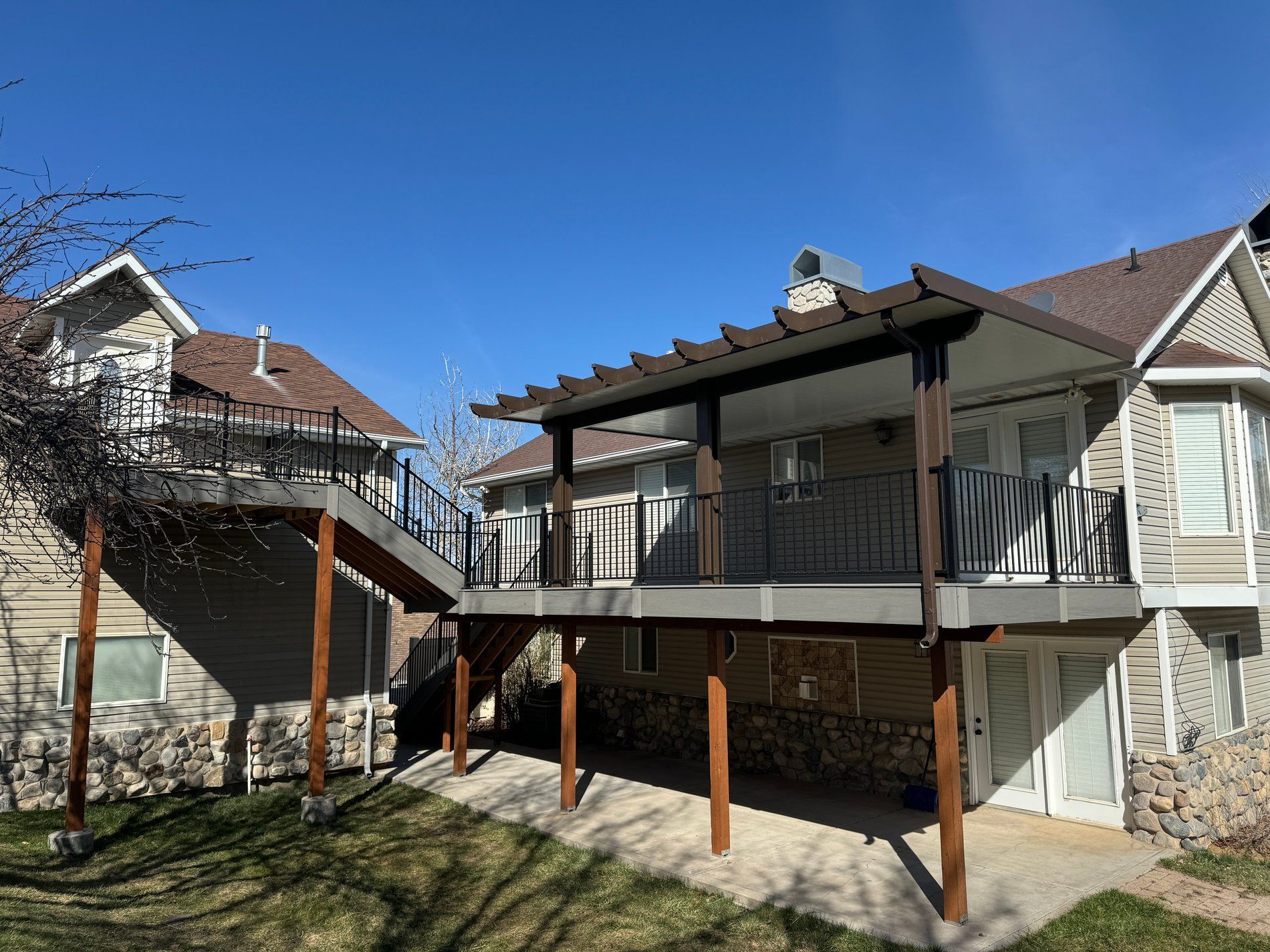 Backyard patio deck with stairs, pergola roof, and wooden support posts beside a house