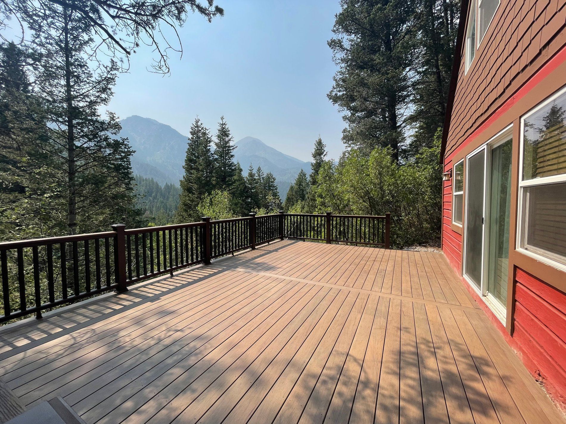 Wooden deck beside a red cabin, overlooking trees and distant mountains on a sunny day