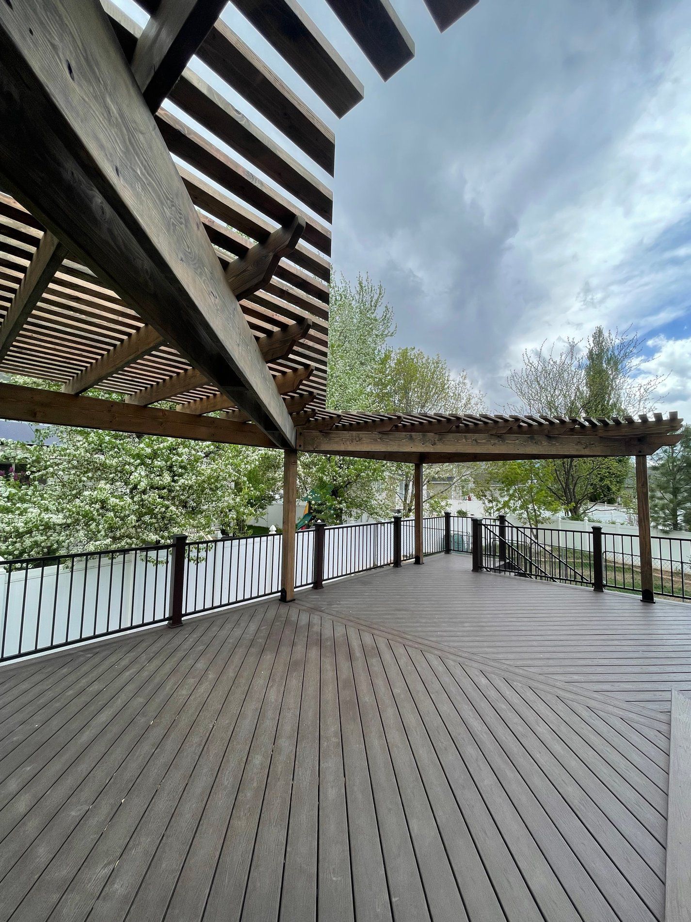Wooden deck under a pergola overlooking a lake and trees on a cloudy day