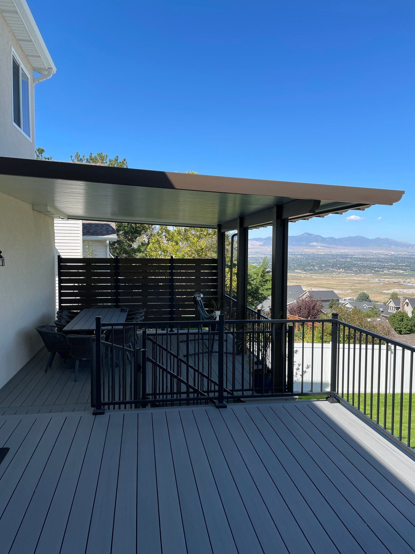 Covered deck with black railing overlooking a valley and distant mountains under a clear blue sky