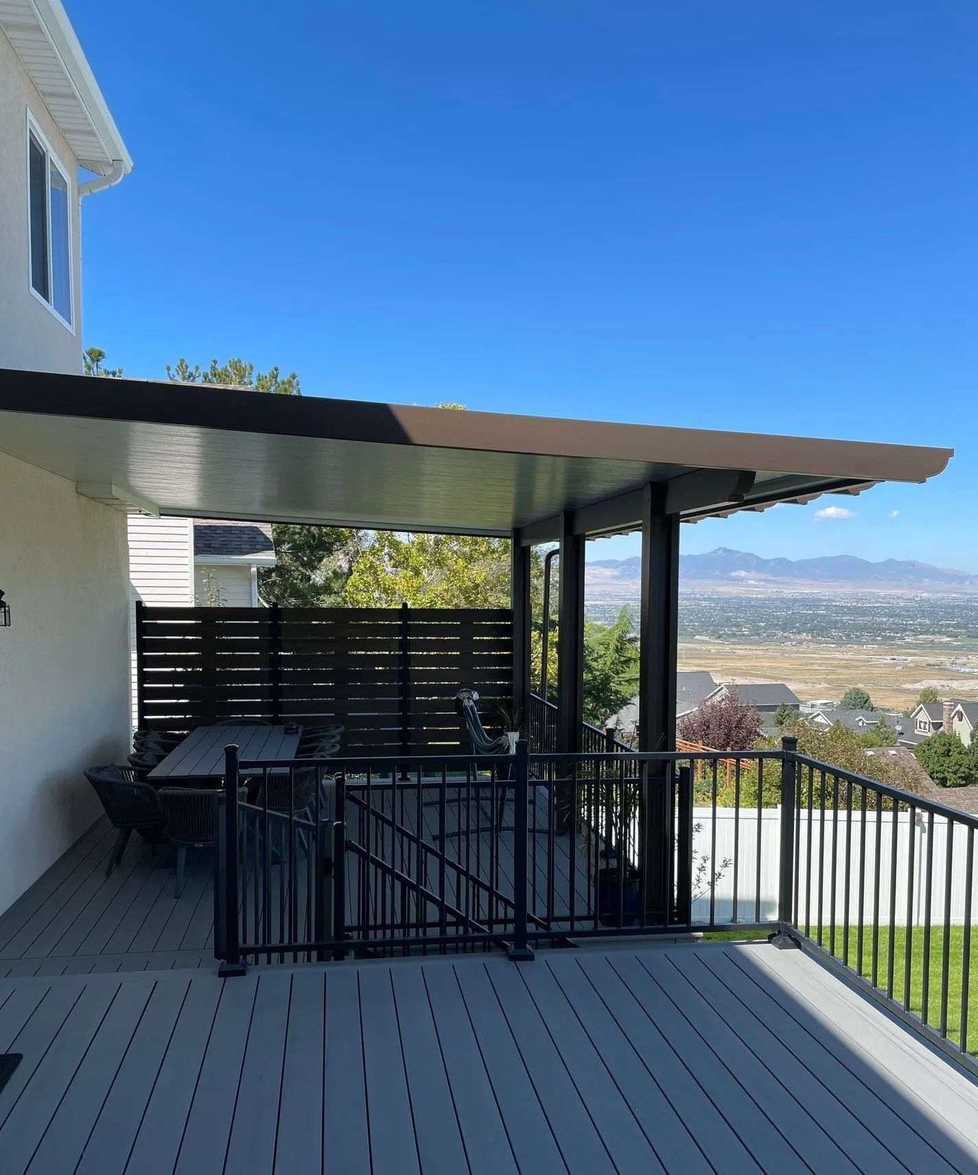 Covered patio with gray decking, black railing, and mountain view under a clear blue sky