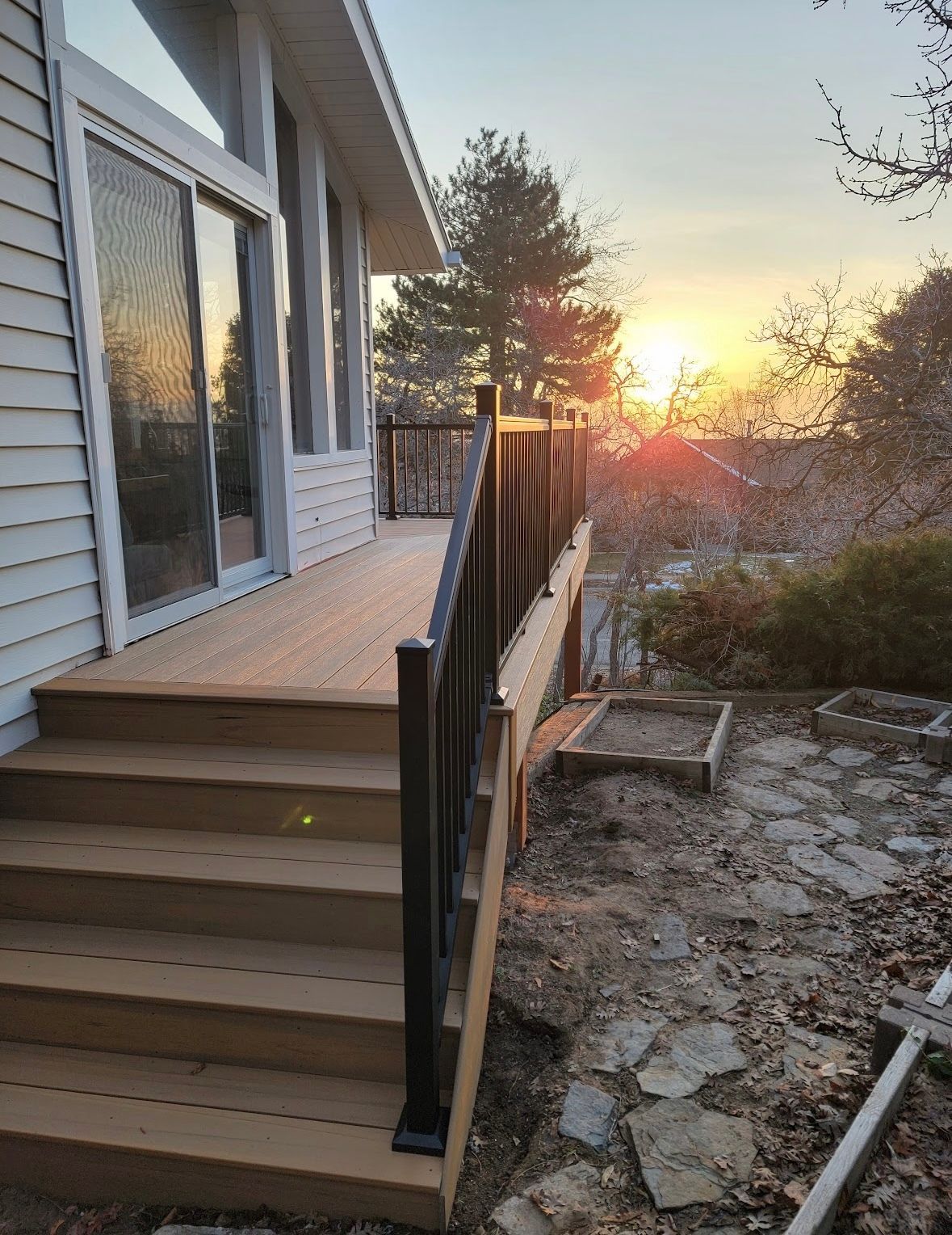Front steps and black railing beside a house, overlooking a rocky yard at sunset.