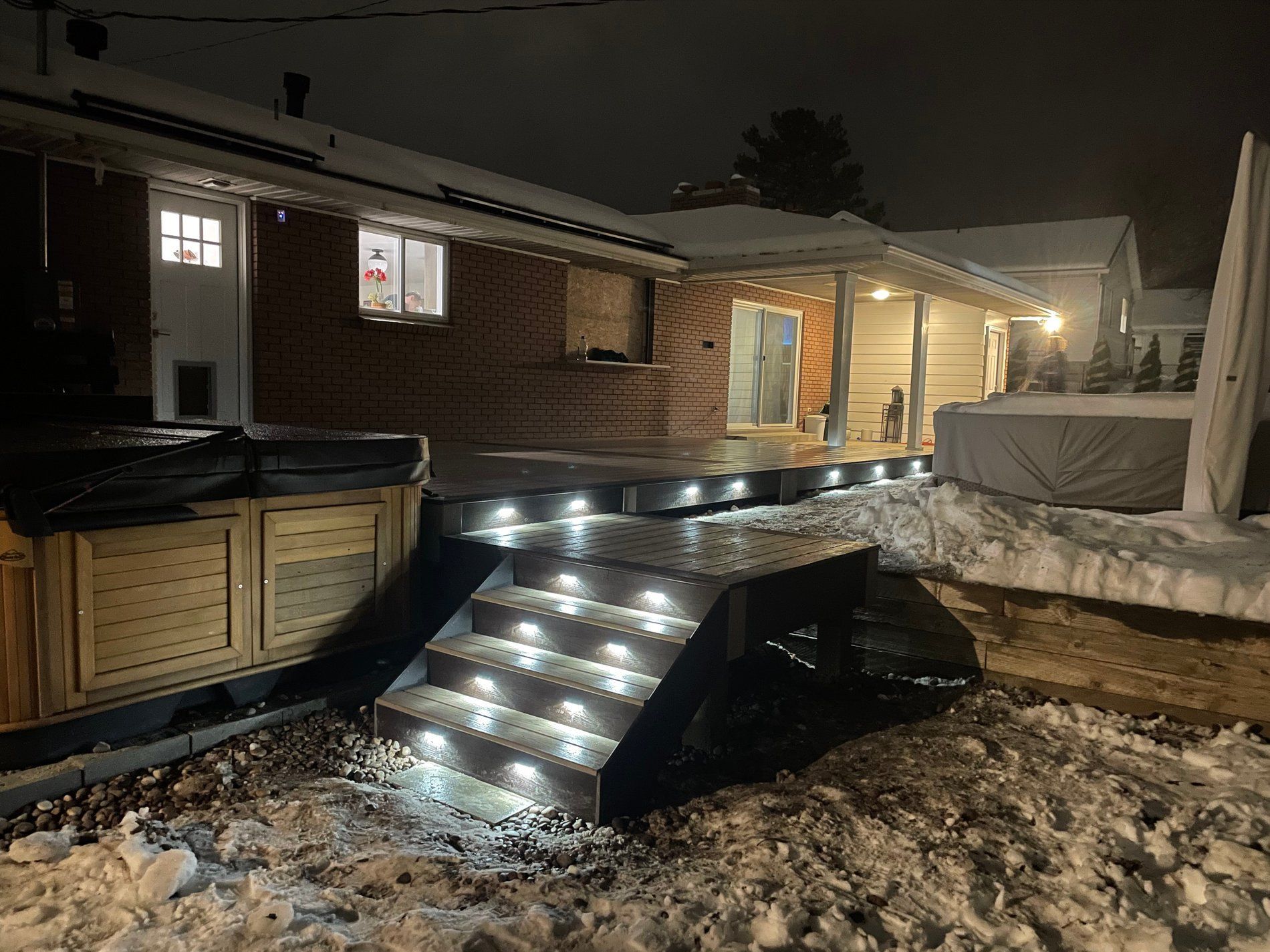 Snowy house deck and stairs lit with string lights at night