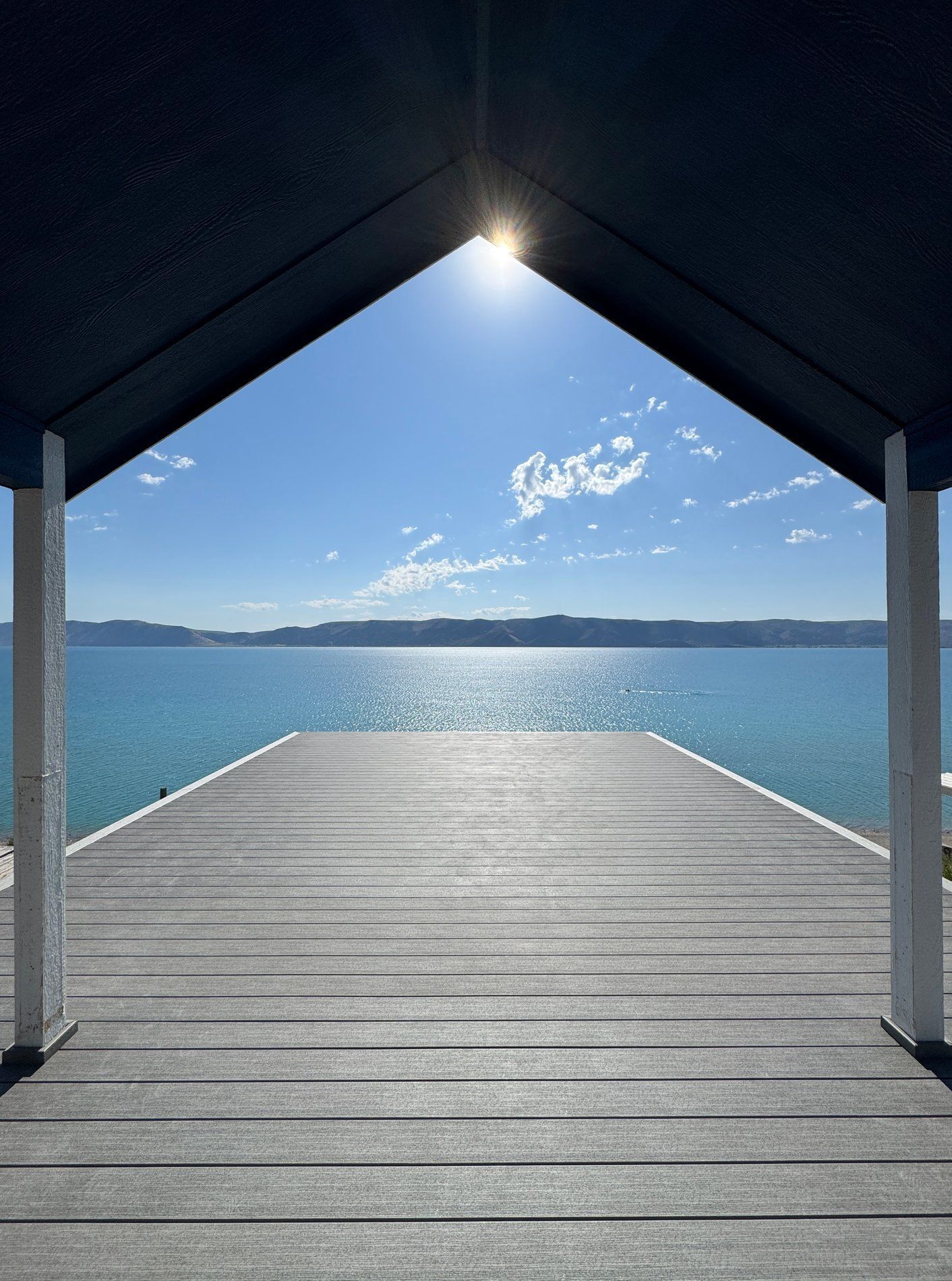 Covered wooden dock extending to calm blue water under a bright sky