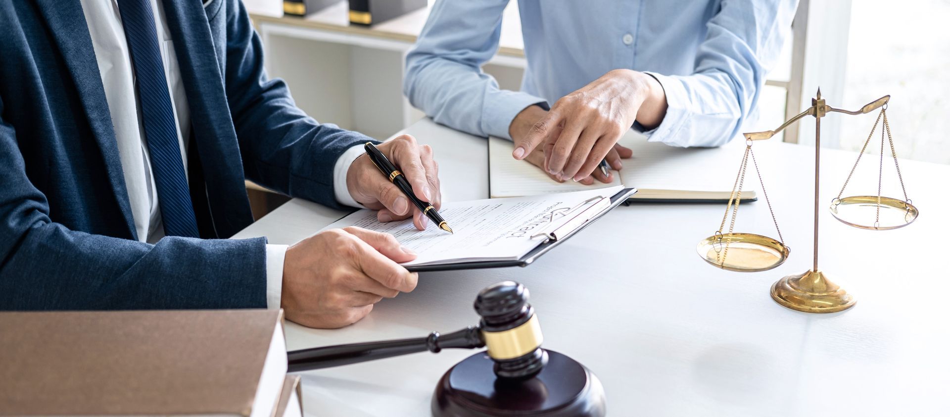 two men are sitting at a table with a gavel and scales of justice