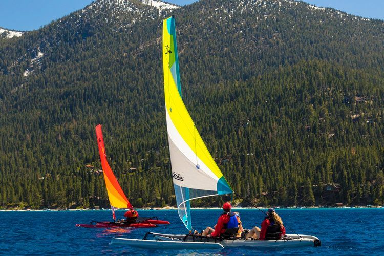 Three people are sailing on a lake with mountains in the background