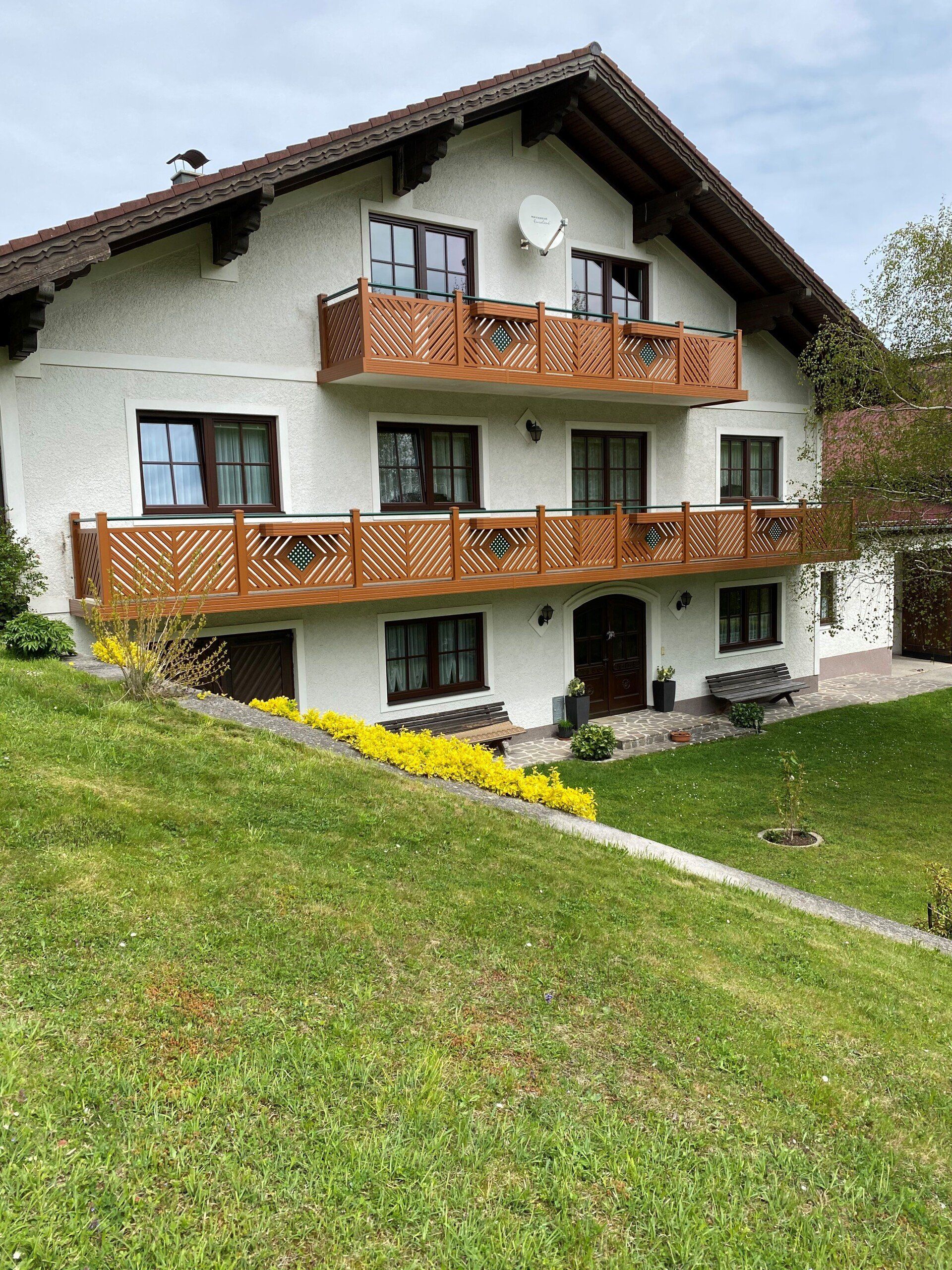 Auf einem grasbewachsenen Hügel steht ein großes weißes Haus mit einem Holzbalkon.