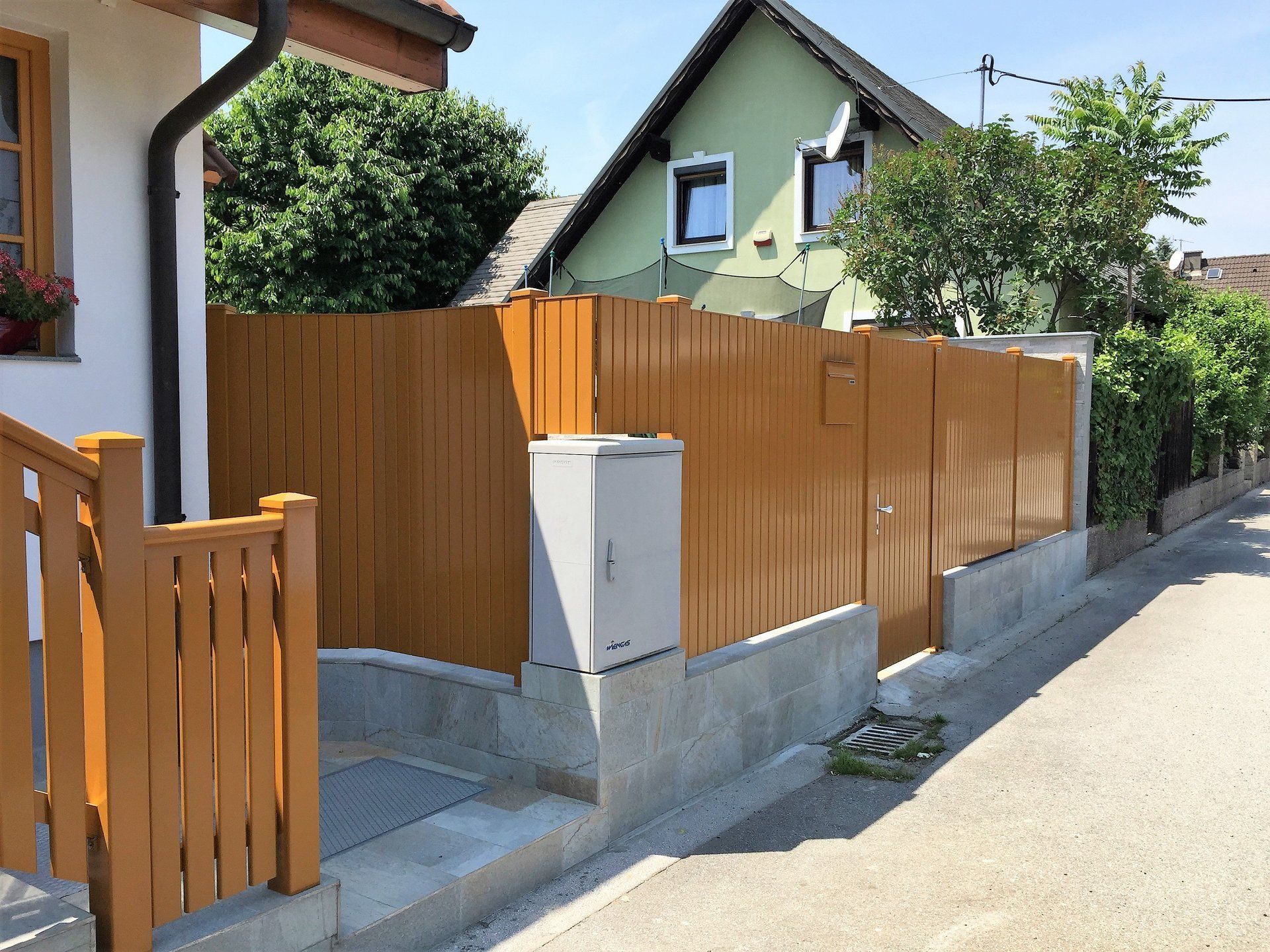Neben einem Haus steht am Straßenrand ein Holzzaun.