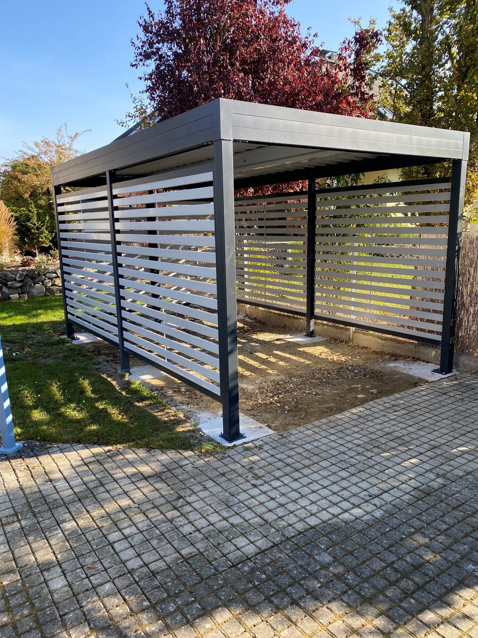 Auf einer gepflasterten Auffahrt steht ein eingezäunter Carport.