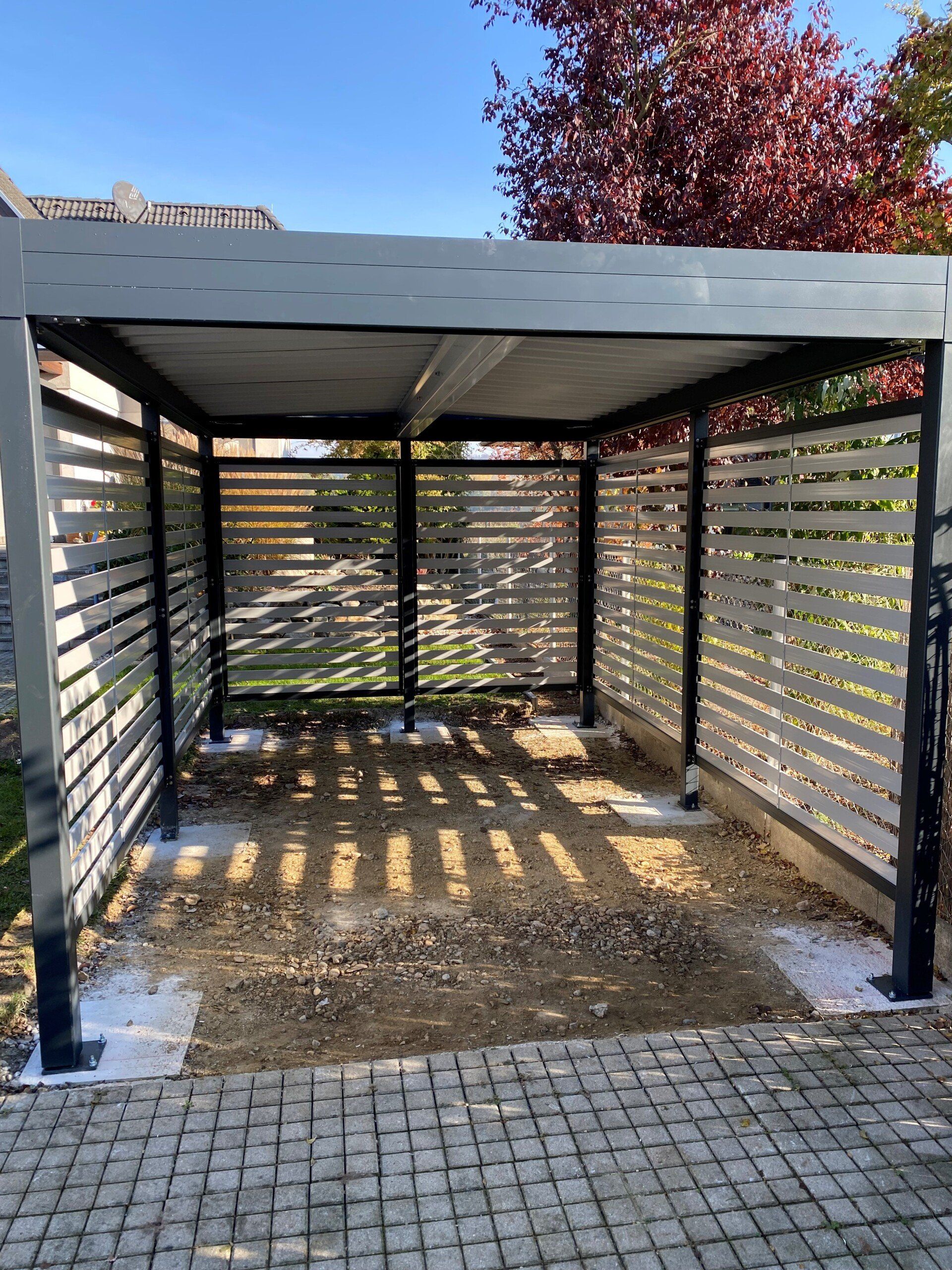 Auf einer gepflasterten Auffahrt neben einem Baum steht ein Carport.