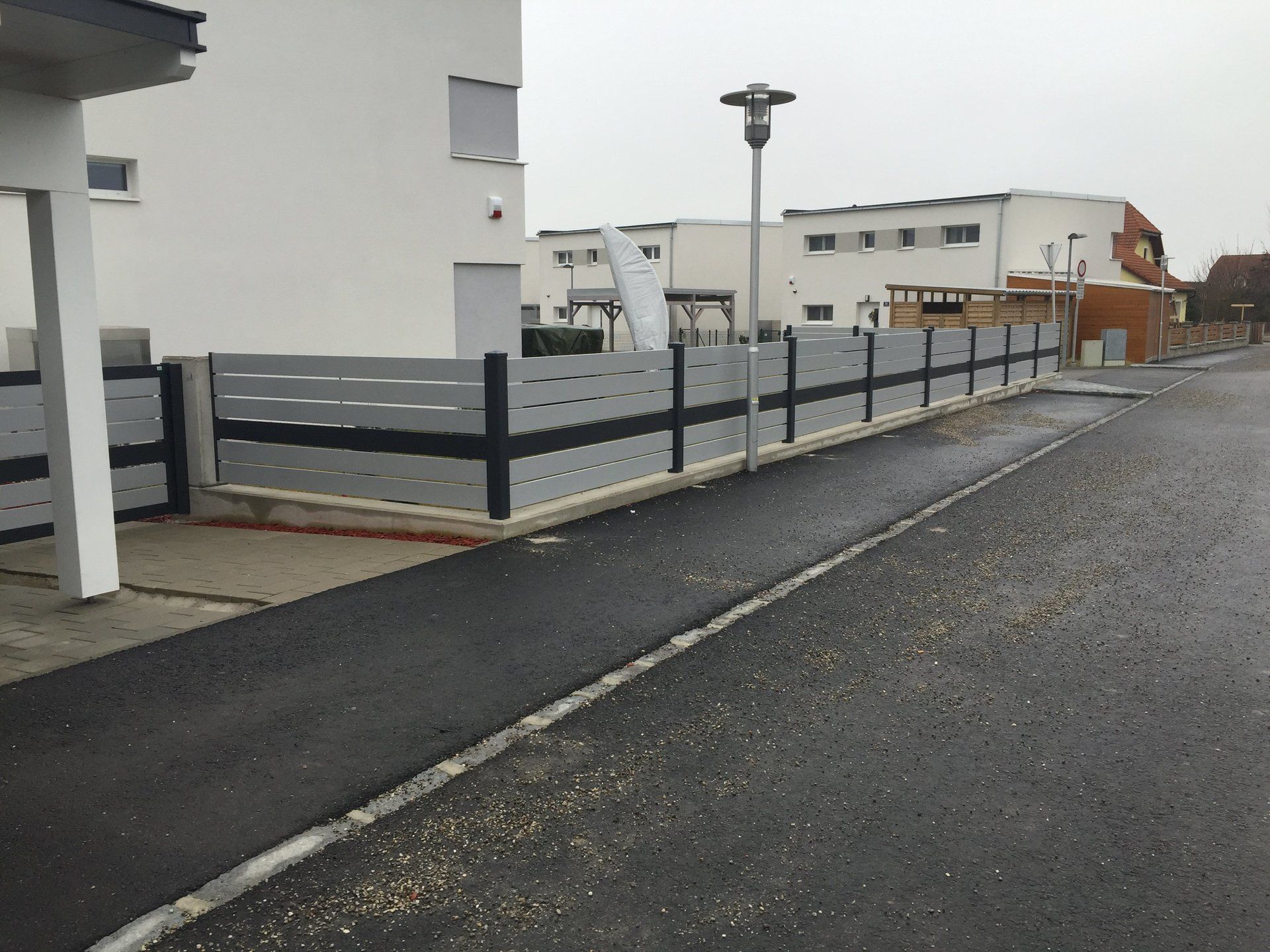 Ein Zaun am Straßenrand vor einem weißen Gebäude