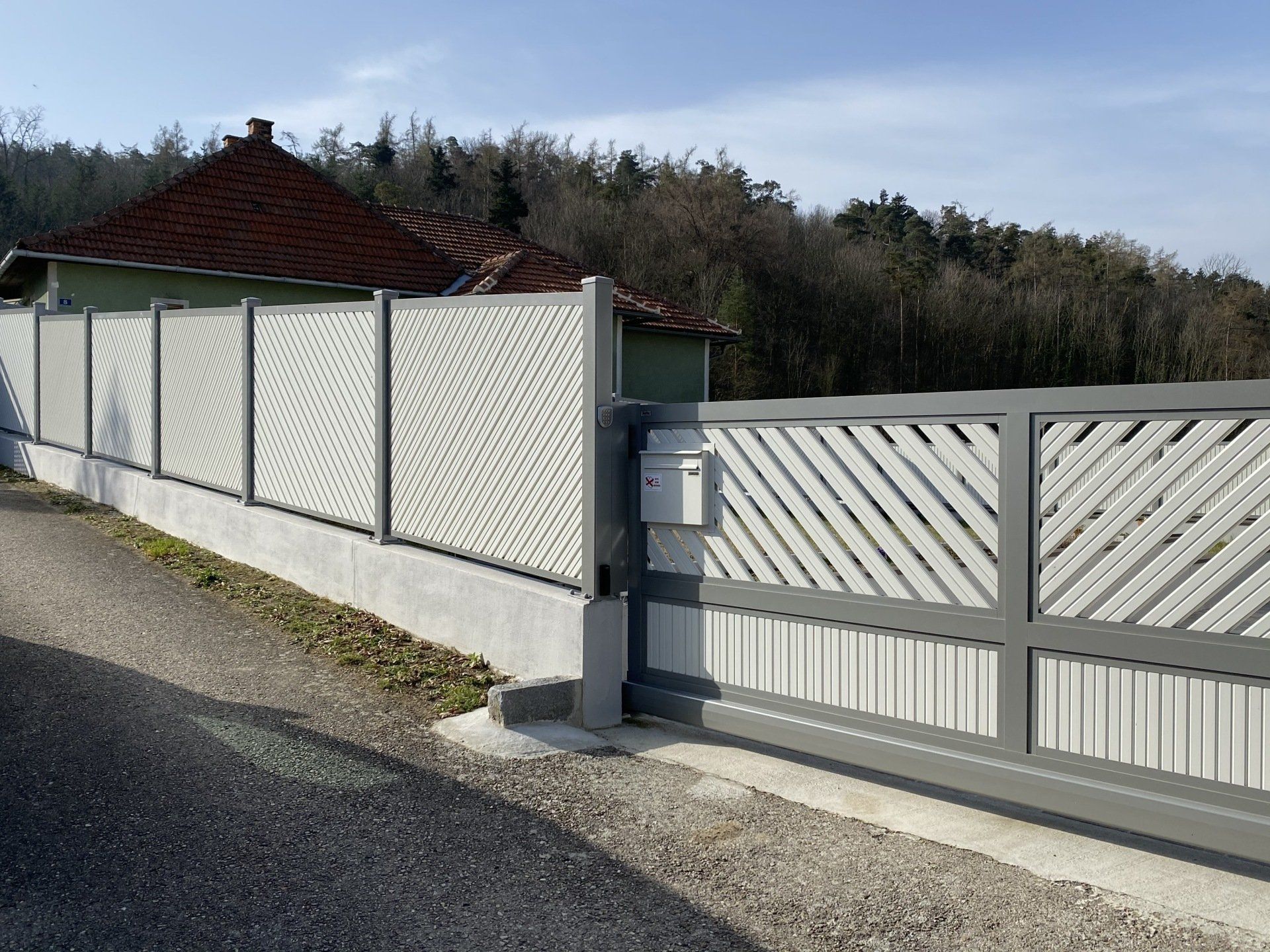Ein weißer Zaun mit einem Schiebetor vor einem Haus.