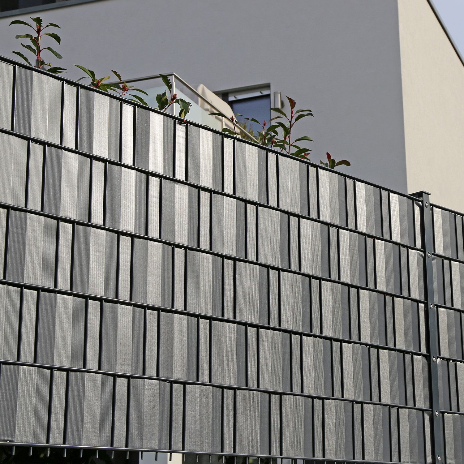 Ein Zaun mit einem grauen Streifen steht vor einem Gebäude