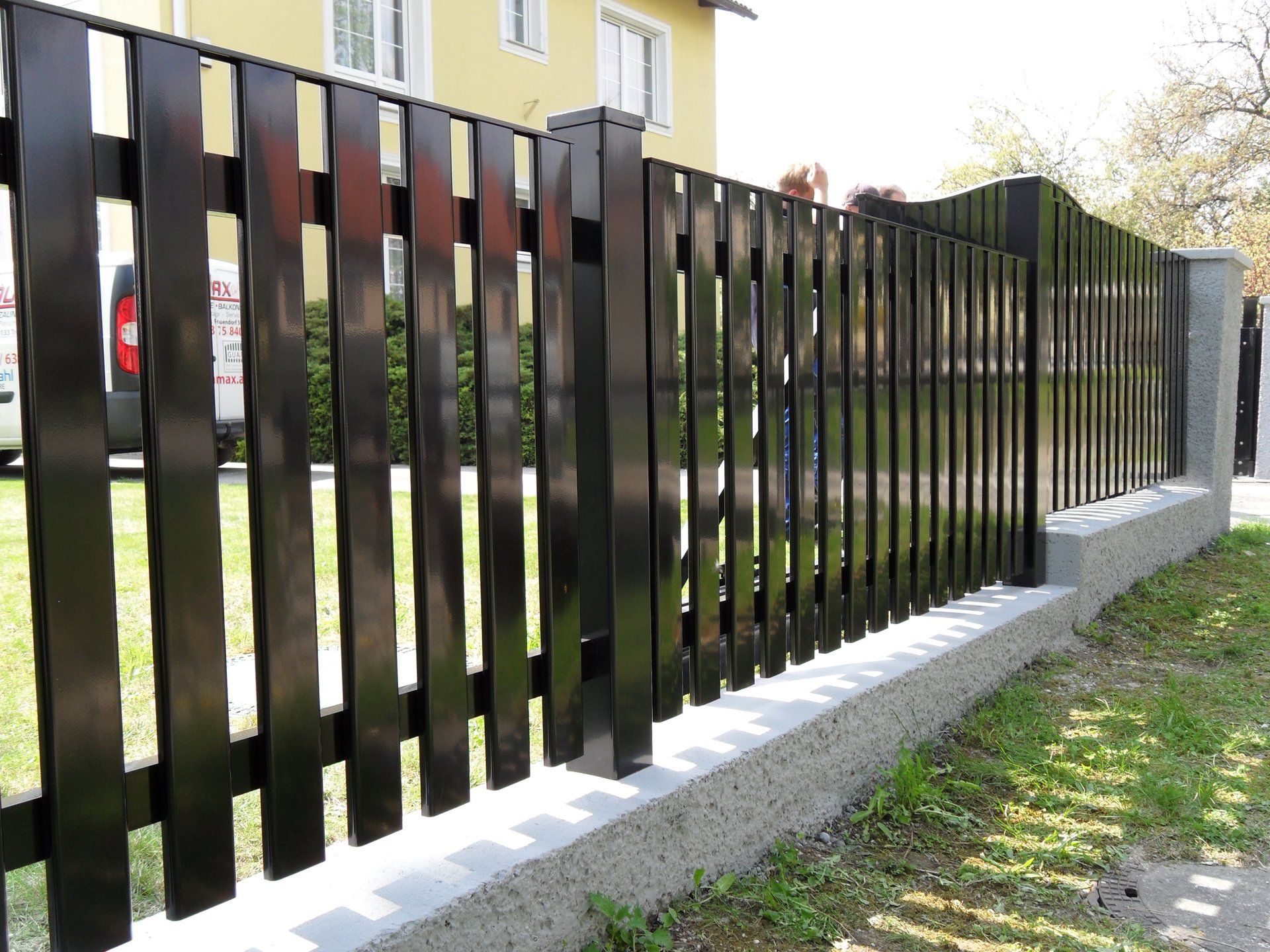 Ein schwarzer Holzzaun mit einem gelben Haus im Hintergrund