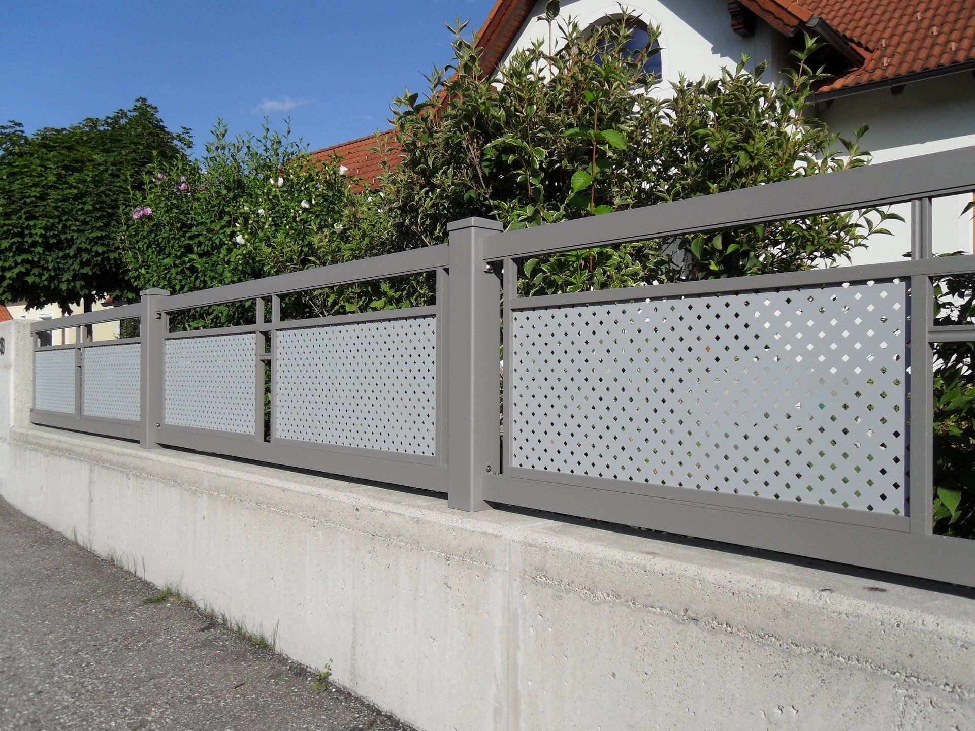 Ein grauer Zaun mit Löchern darin steht neben einem Haus