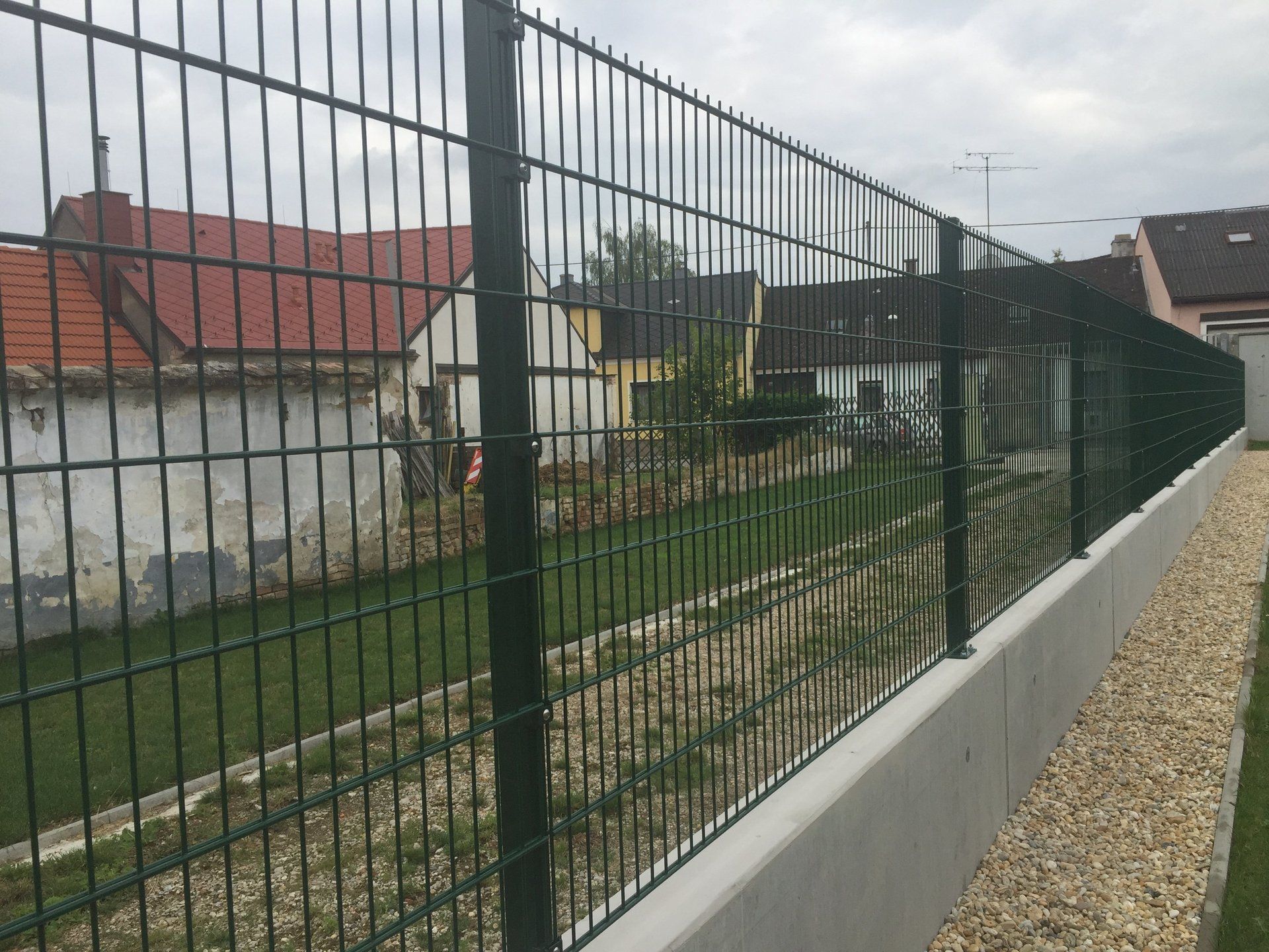 Ein schwarzer Zaun umgibt eine Kiesauffahrt mit Häusern im Hintergrund