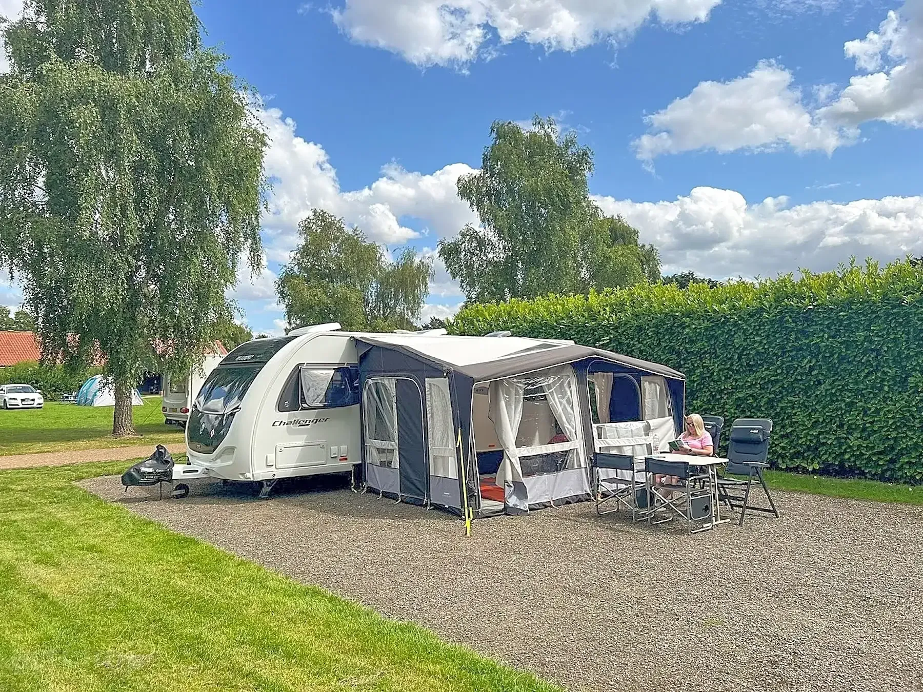 Caravan with awning set up at a campsite on a sunny day.