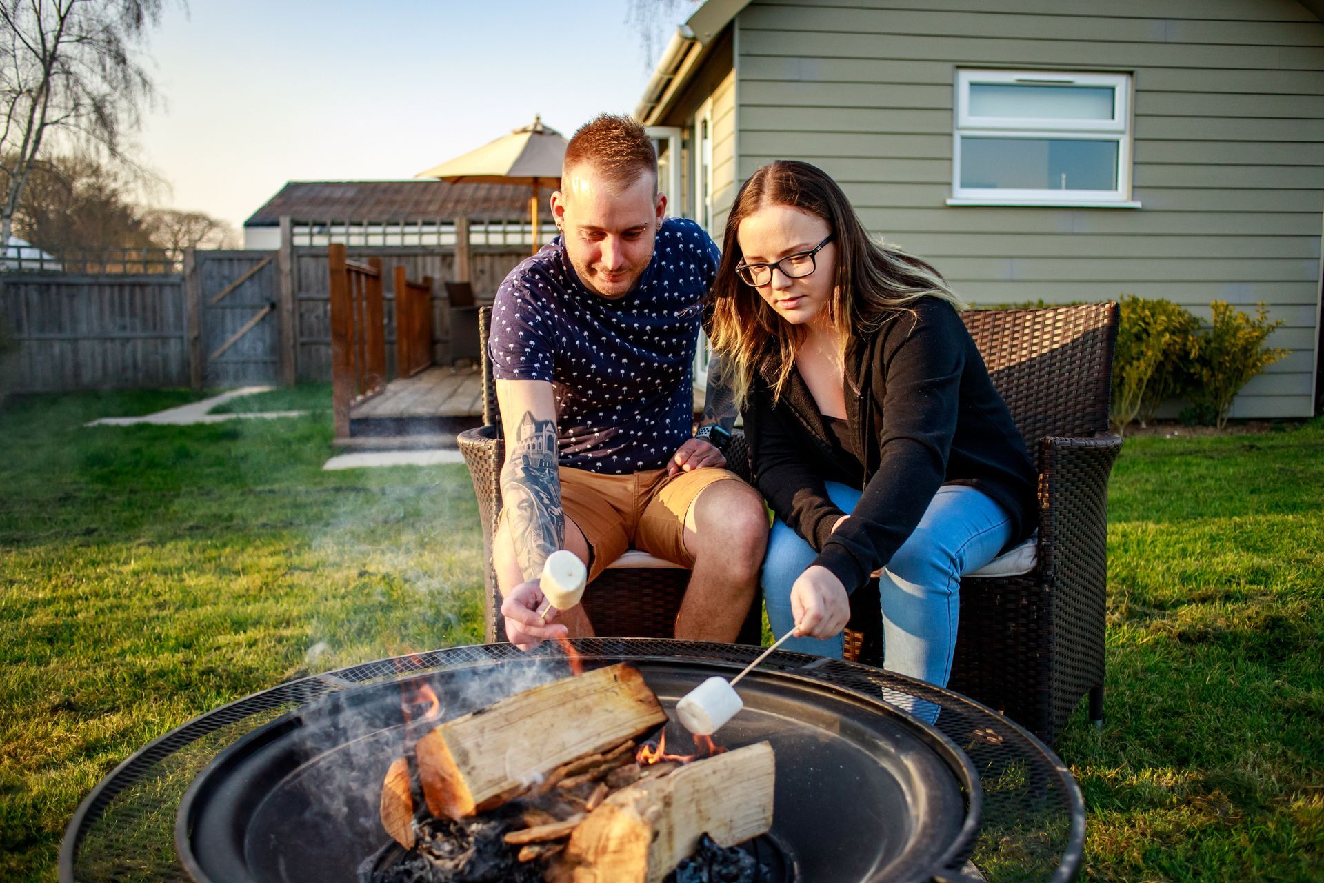 Couple roasting marshmallows over a fire pit in backyard.