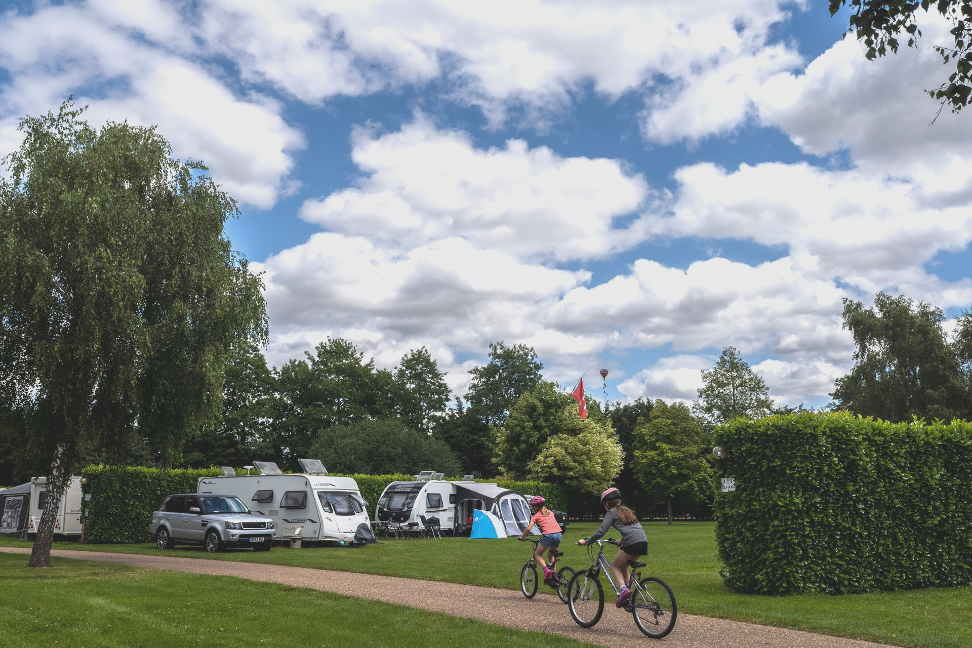 Campground with RVs and cyclists under a cloudy blue sky.