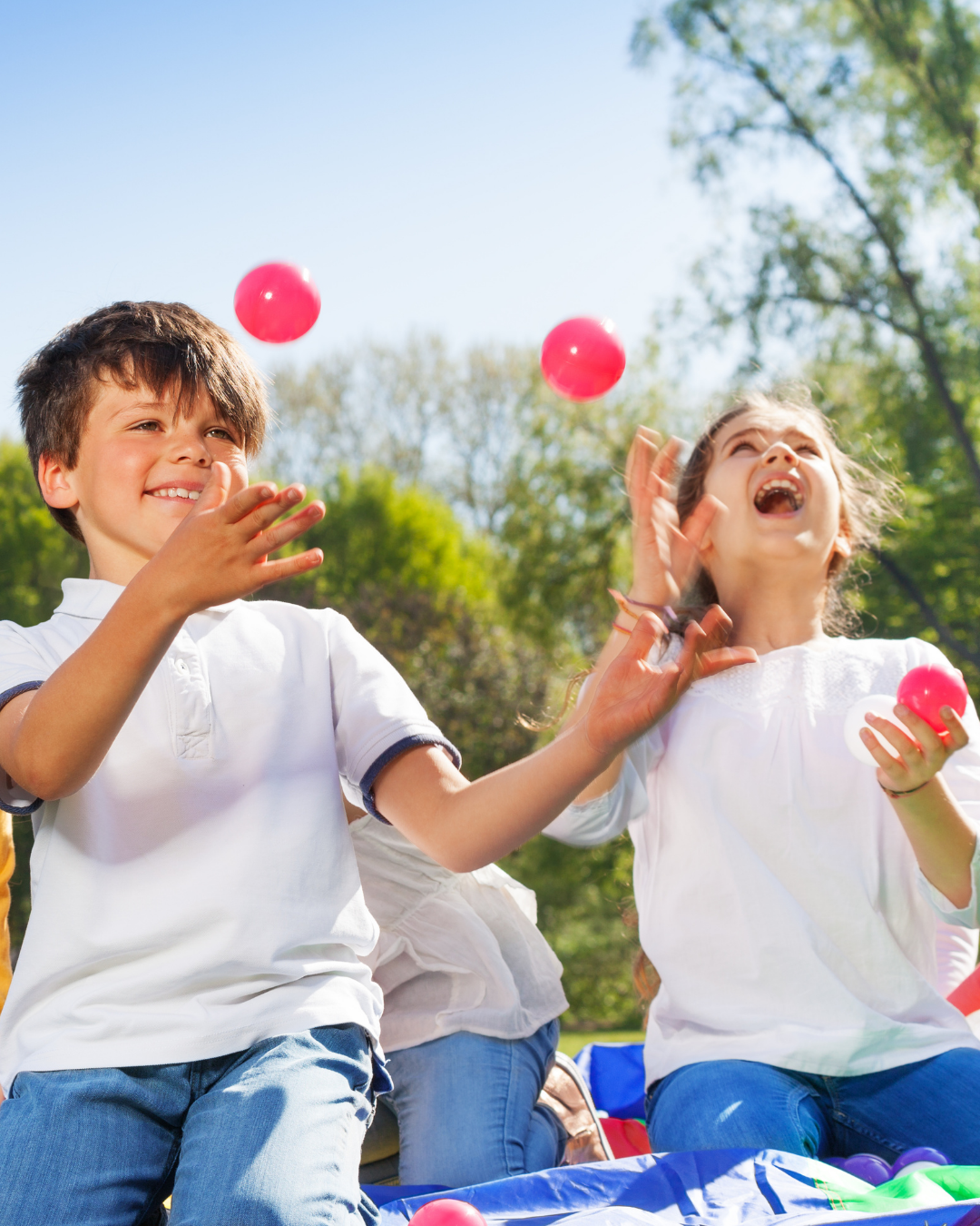 Two children learning to juggle with red balls in a sunny outside setting