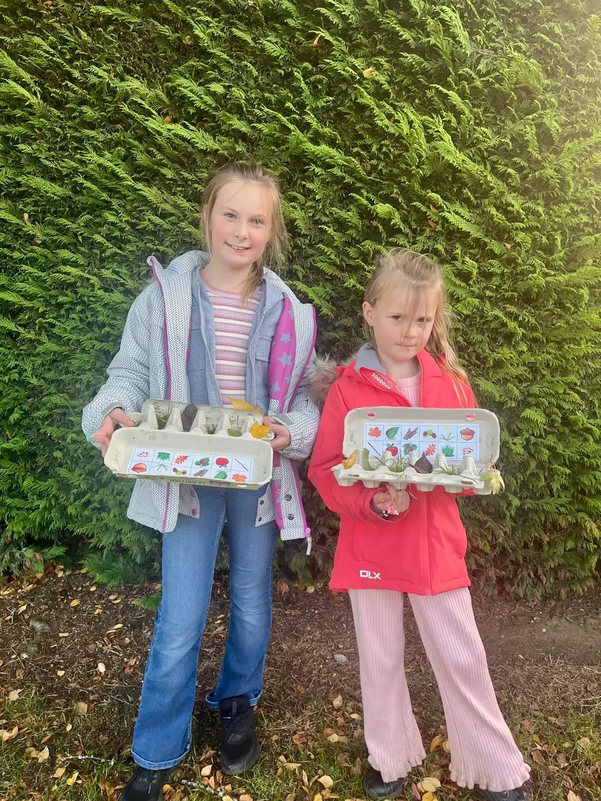 Two children holding egg boxes filled with leaves, flowers and other natural finds collected during an autumn scavenger hunt at Applewood Countryside Park.