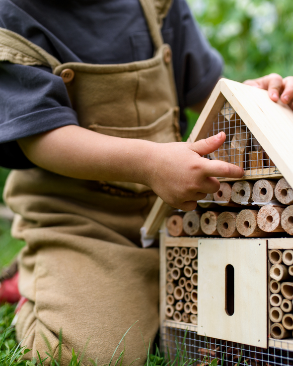 Child wearing dungarees putting the finishing touches to a wooden bug hotel