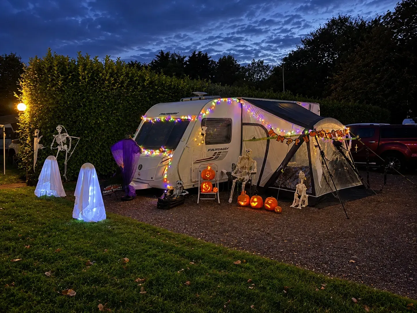 Halloween-decorated caravan at Applewood Countryside Park, lit with colourful lights, glowing pumpkins, ghosts and skeletons at dusk.