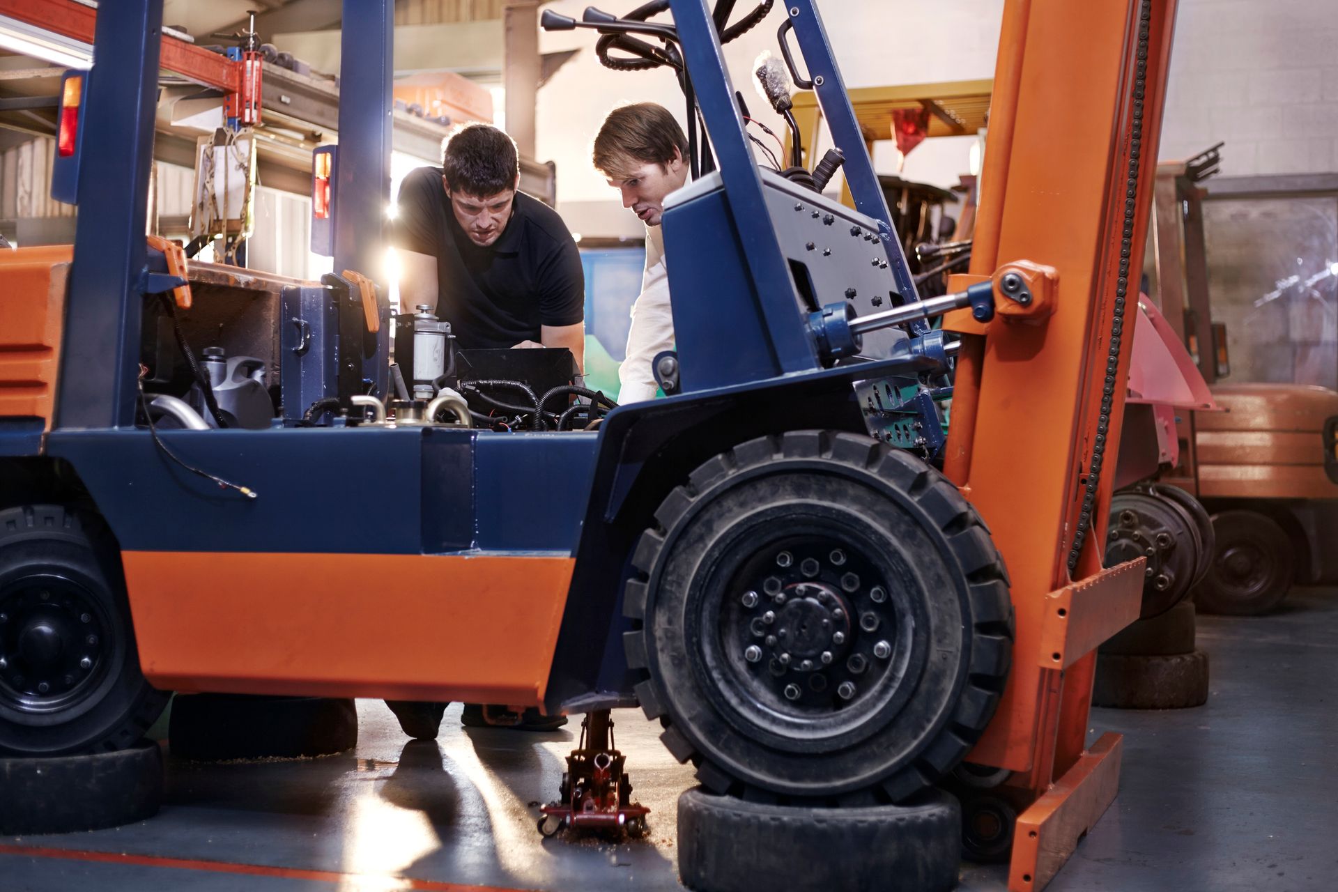 Two men are working on a forklift in a garage.