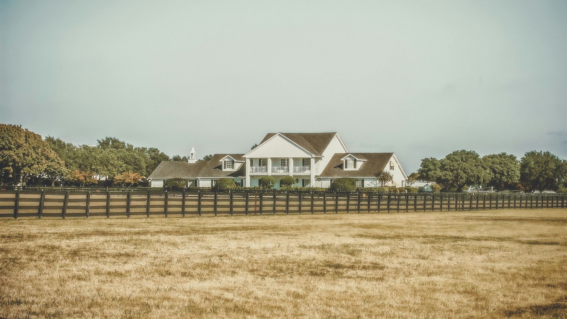 A large white house is behind a wooden fence in a field.