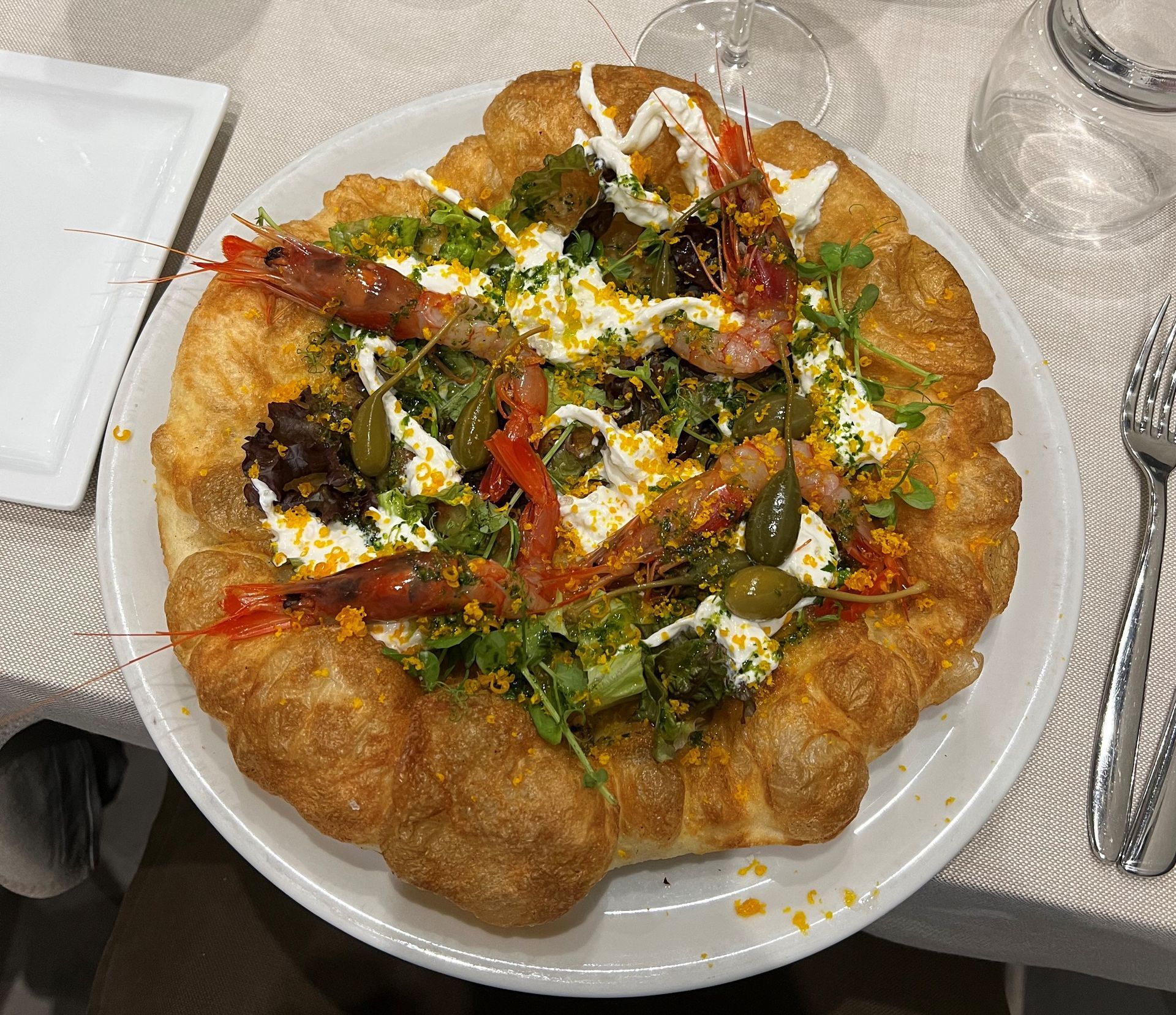 Una pizza con gamberi e olive su un piatto bianco