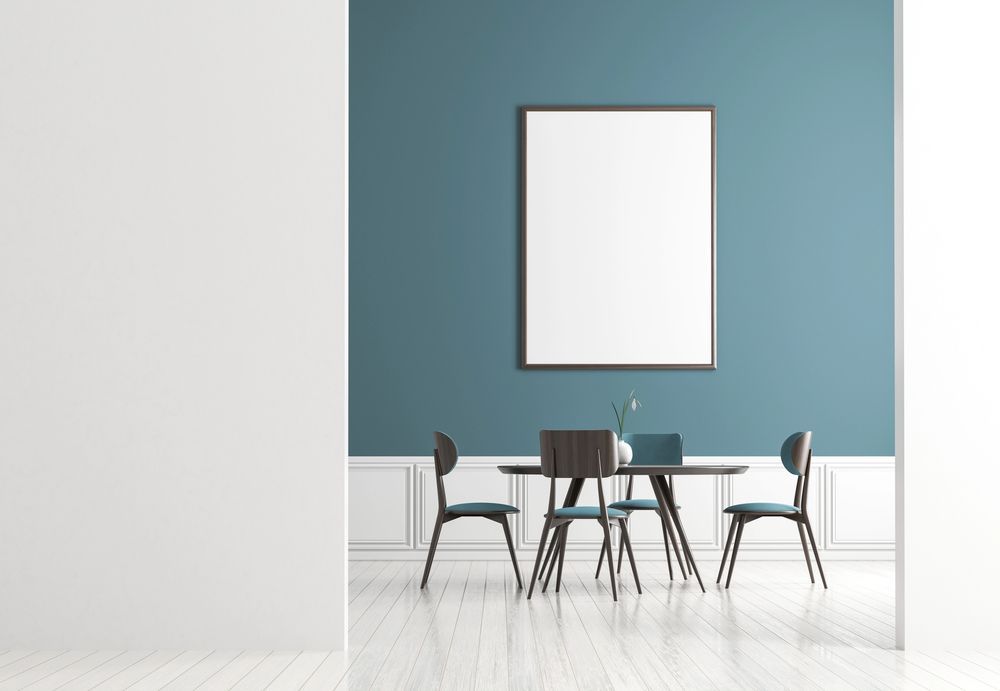 Sala da pranzo minimalista con parete d'accento blu, quadri incorniciati e sedie nere attorno a un tavolino.