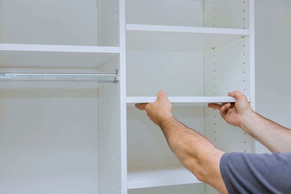 Mani che installano una mensola bianca all'interno di un armadio vuoto.