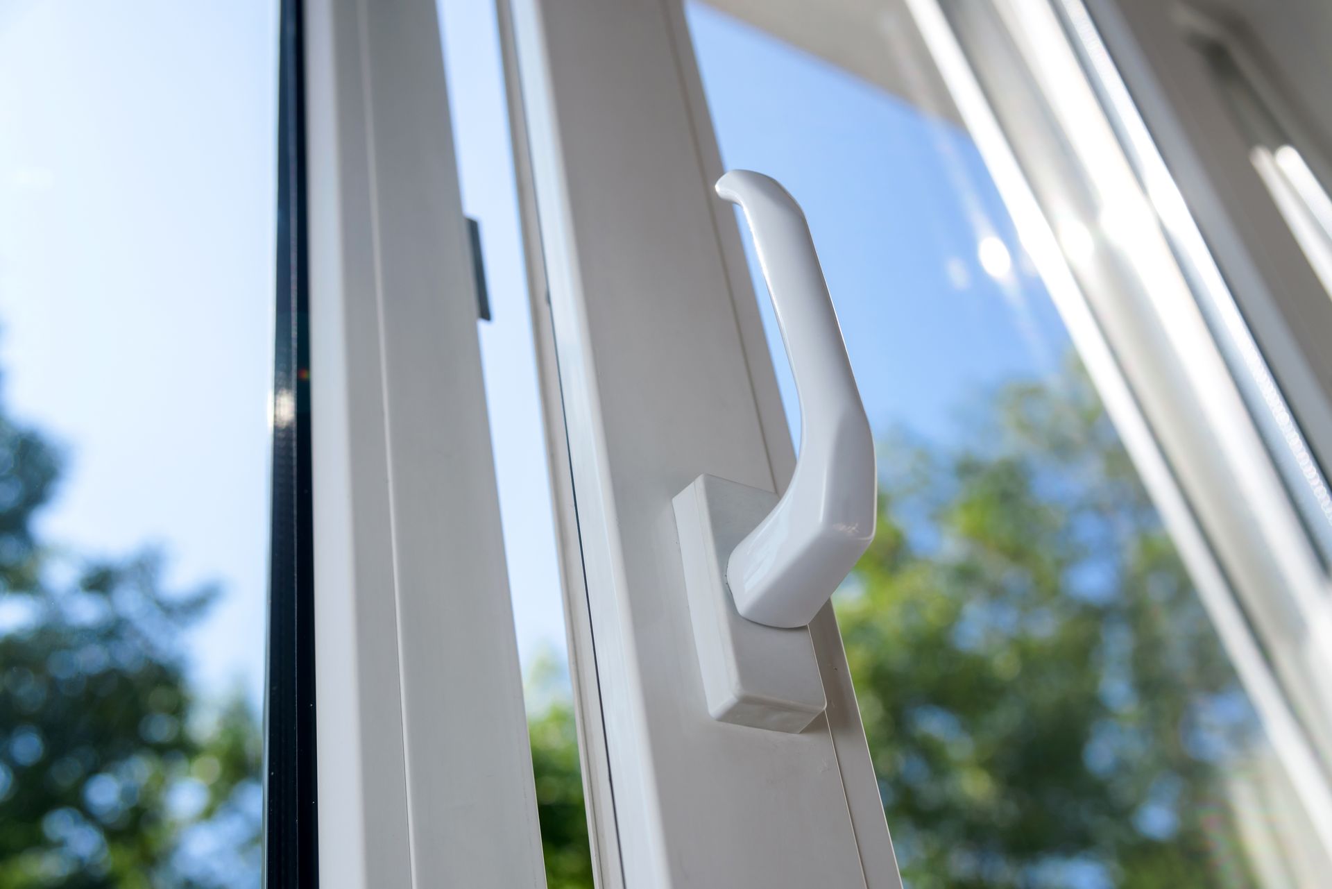 Close-up of a white window handle on a sunlit glass window.