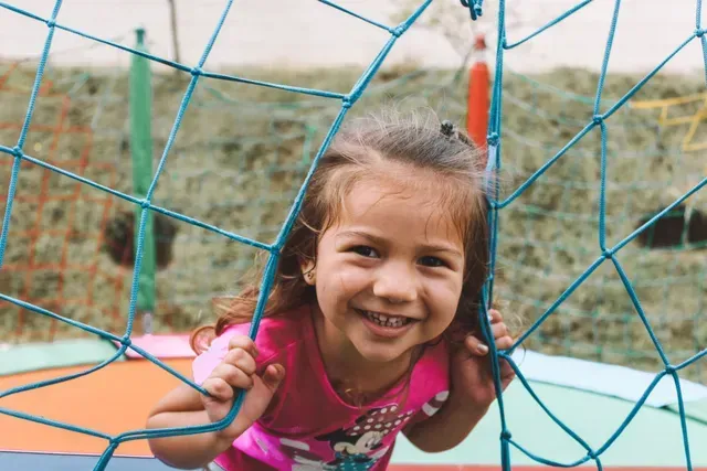 Smiling young girl lying on her stomach on a bed with her hand under her chin. She is holding a toy.