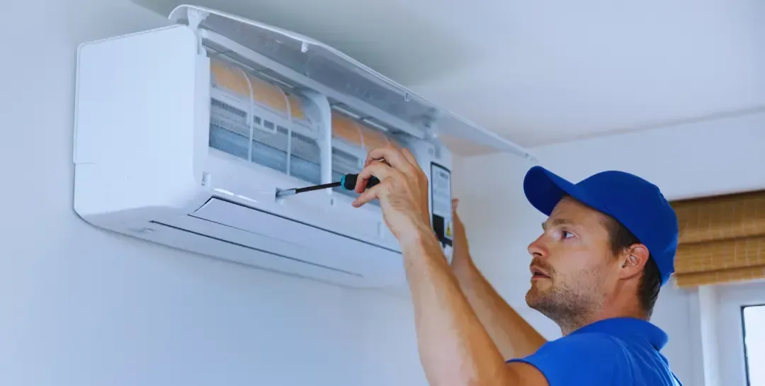 A man is fixing an air conditioner with a screwdriver.