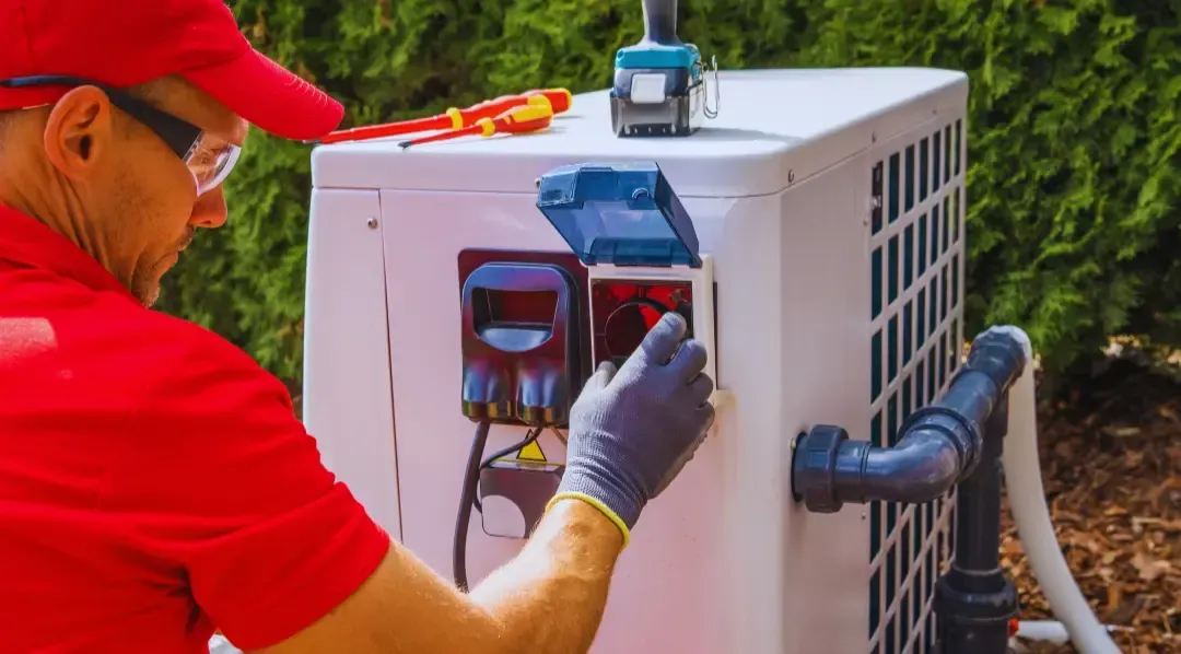 A man in a red shirt is working on an air conditioner outside.