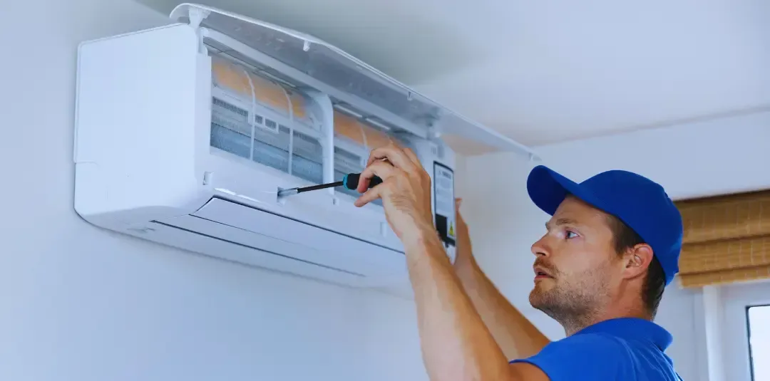 A man is fixing an air conditioner with a screwdriver.