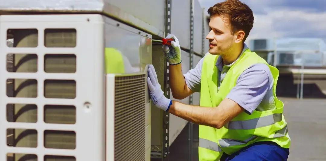 A man in a yellow vest is working on an air conditioner.