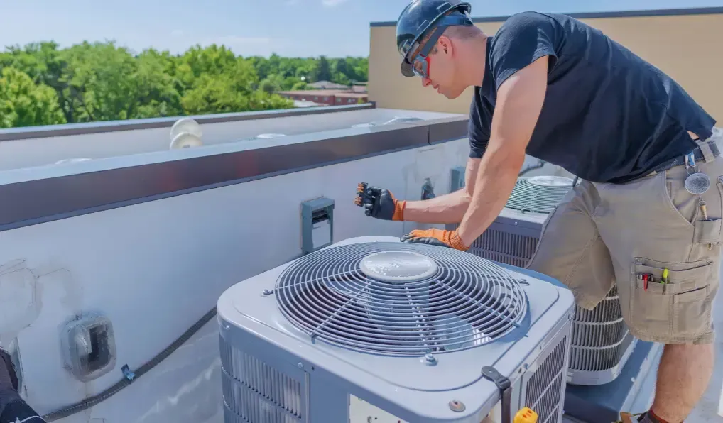 A man is working on an air conditioner on the roof of a building.