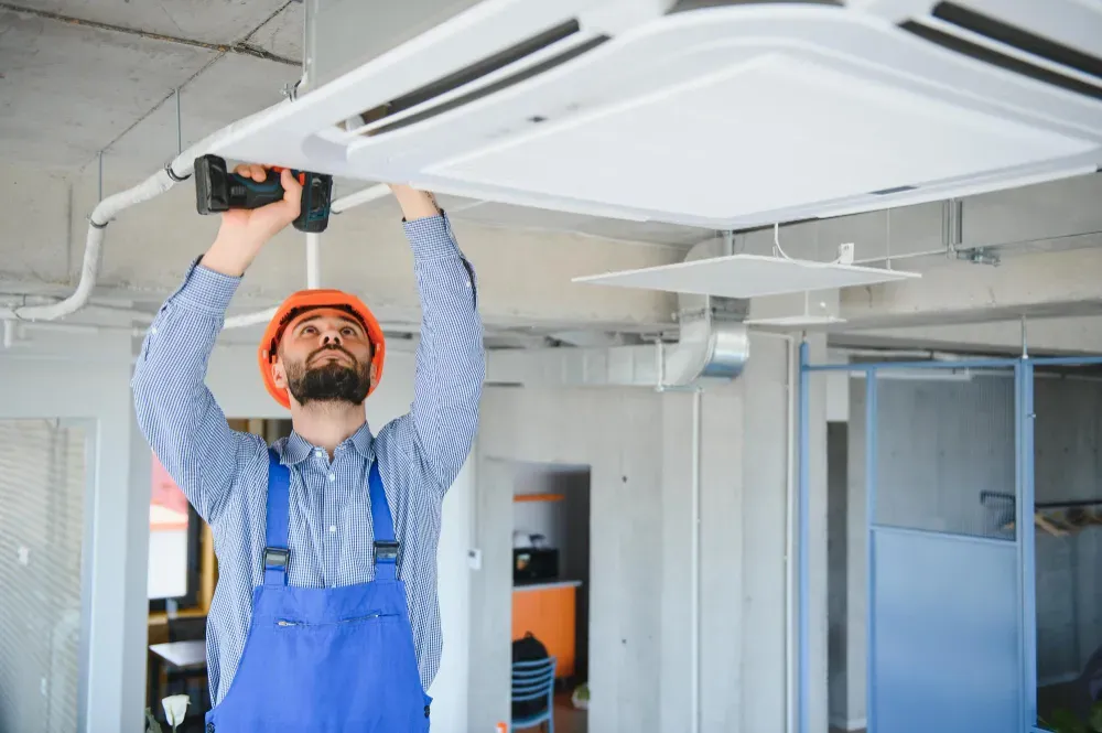 Hvac services - A man is installing a ceiling fan in an office.