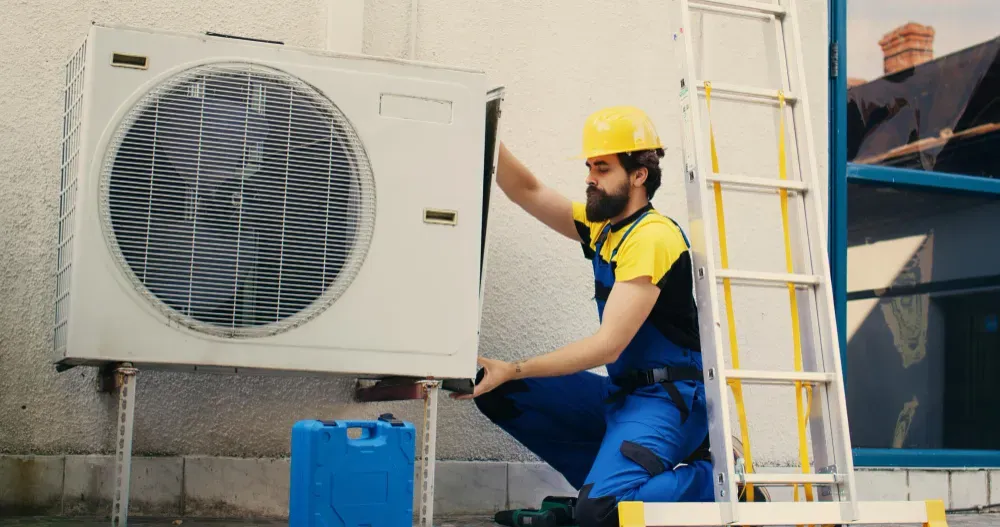Hvac Services - A man is installing an air conditioner on the side of a building.
