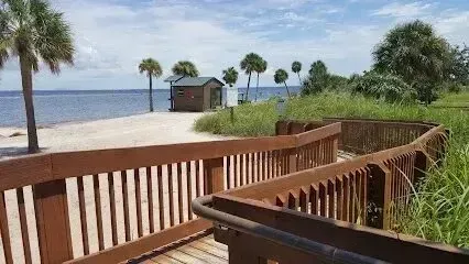 Hvac-Contractor-Bradenton-Wooden boardwalk leading to a sandy beach with palm trees and a small building. Ocean in the background.