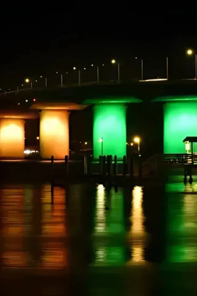 HVAC-contactor-bradenton-Bridge illuminated with green, orange, and yellow lights reflecting on the water at night.