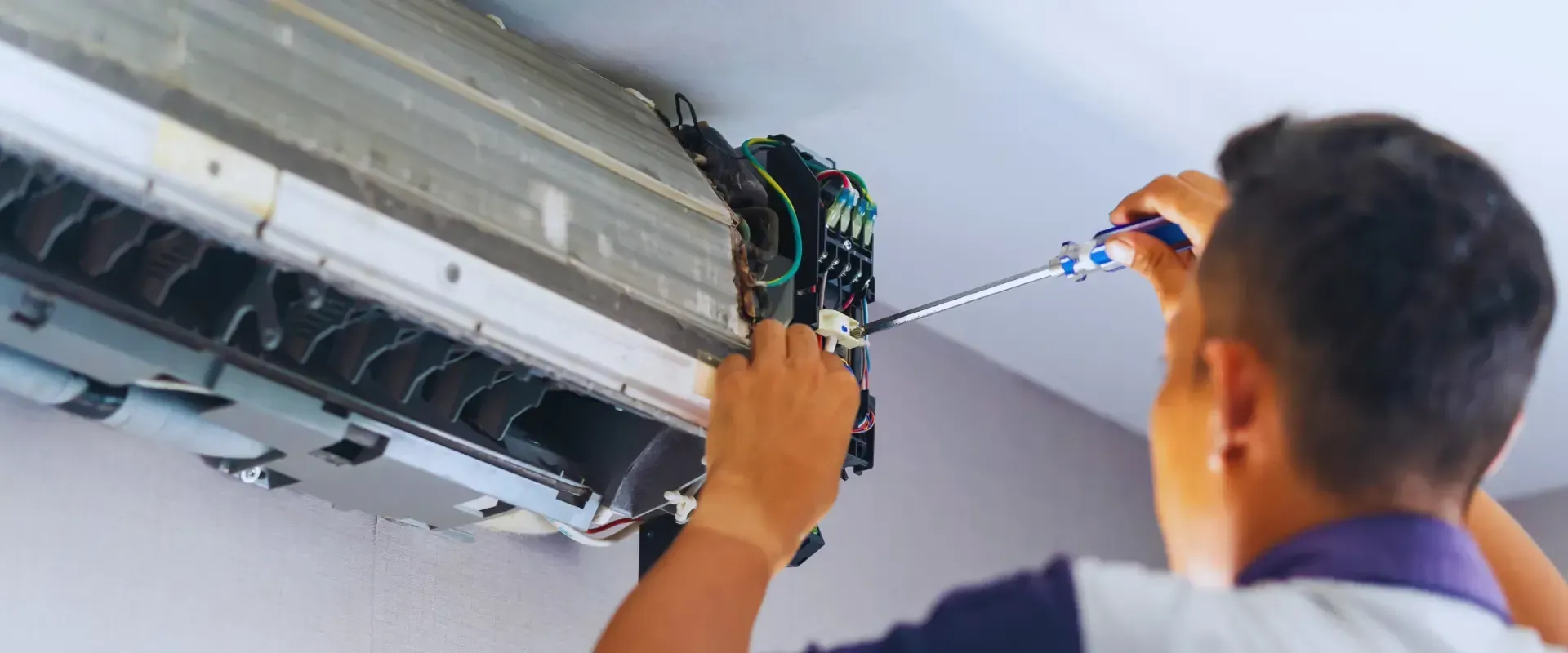A man is fixing an air conditioner with a screwdriver.